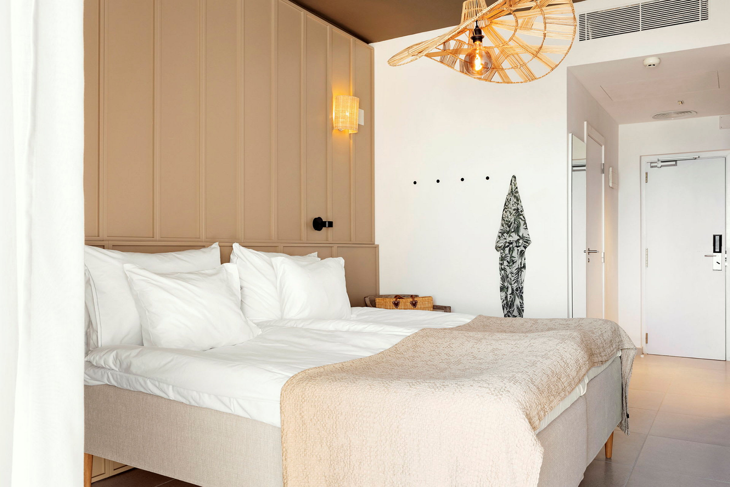 Ett hotellrum med en dubbelsäng, vita väggar och en ljus inredning. (AI-genererad text)