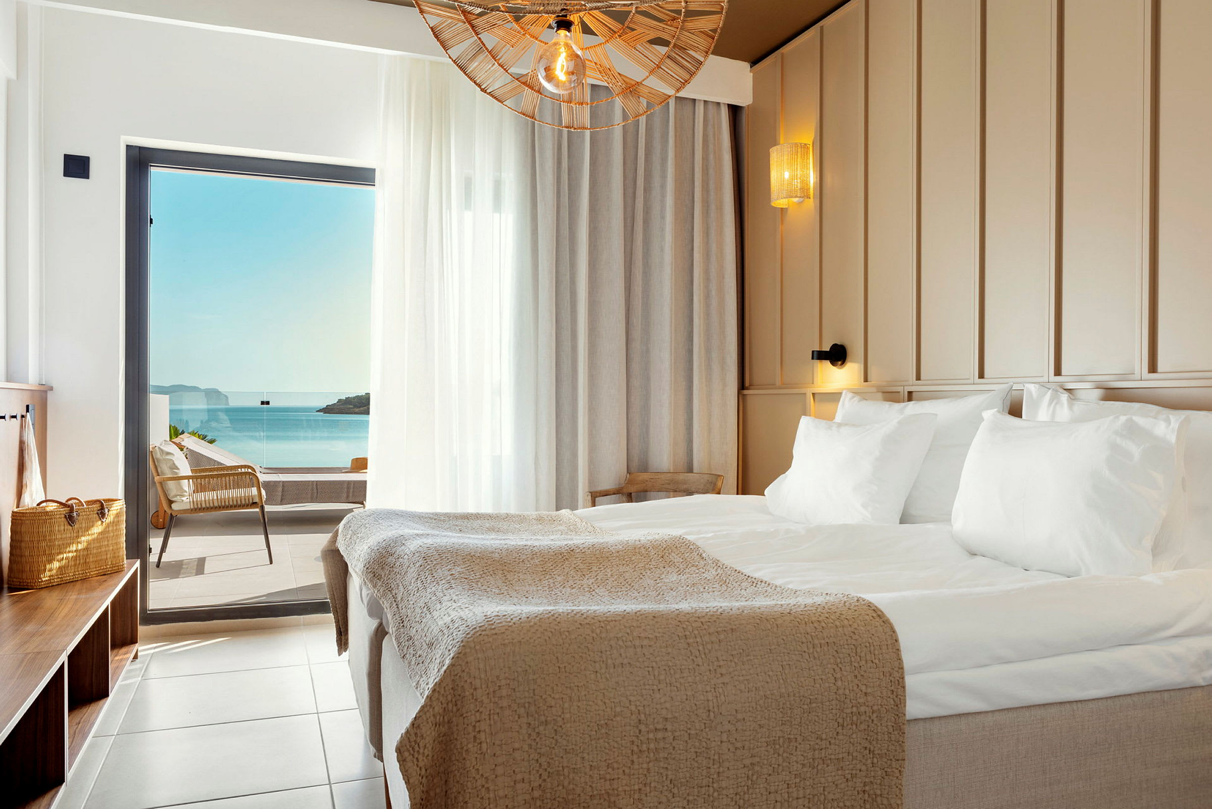 Ett hotellrum med en stor säng och havsutsikt genom en balkongdörr. (AI-genererad text)
