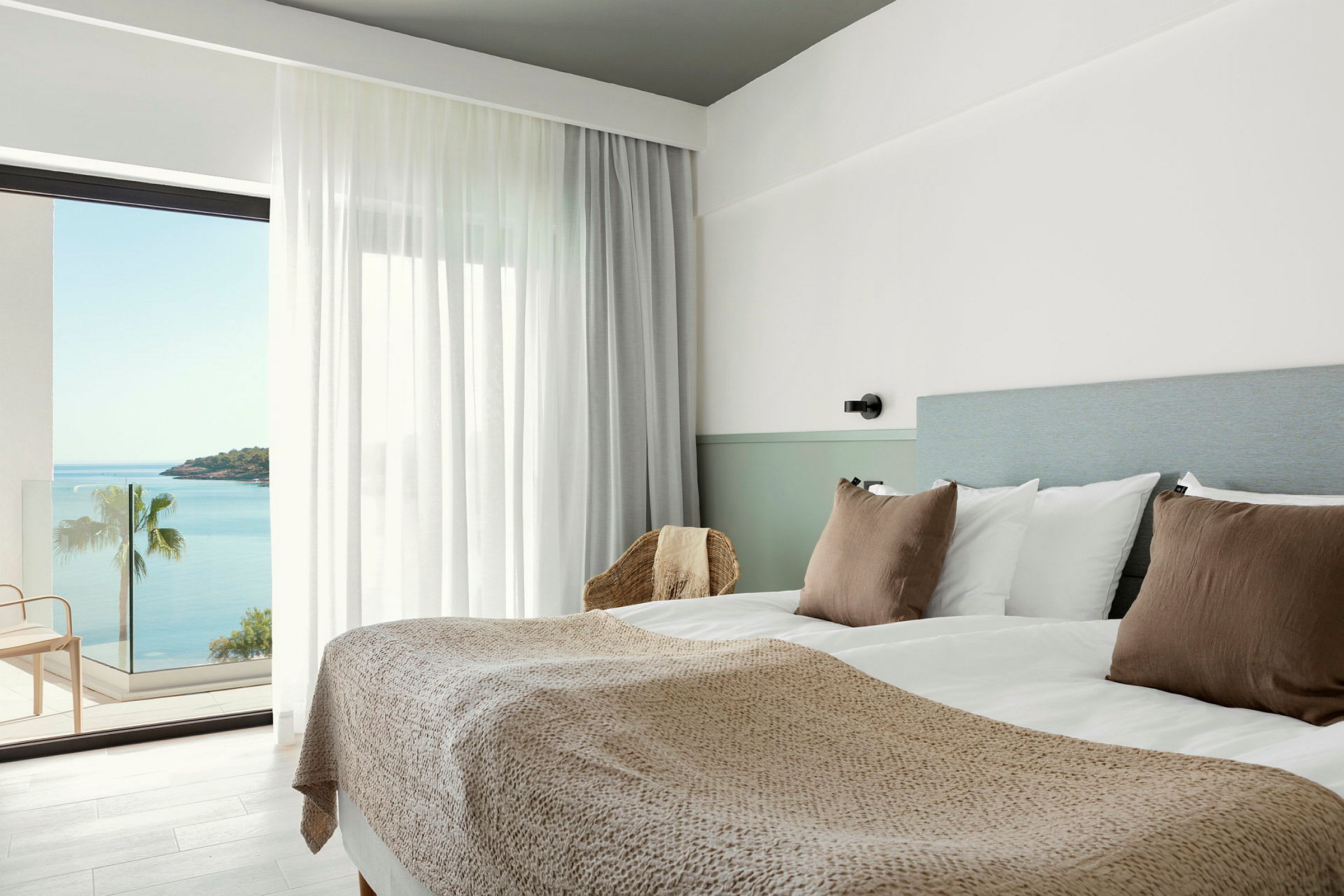 Hotellrum med dubbelsäng, ljusa färger och havsutsikt från balkongen. (AI-genererad text)