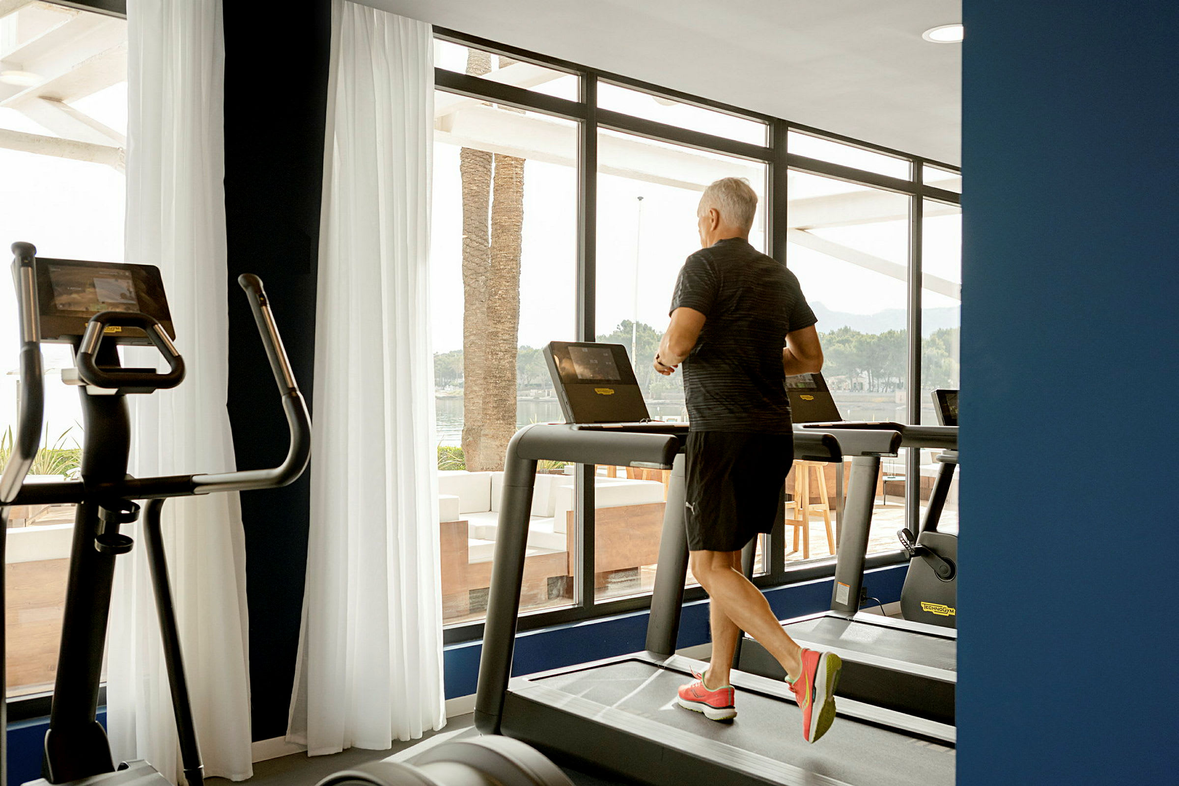 En person springer på ett löpband i ett gym som har stora fönster. (AI-genererad text)