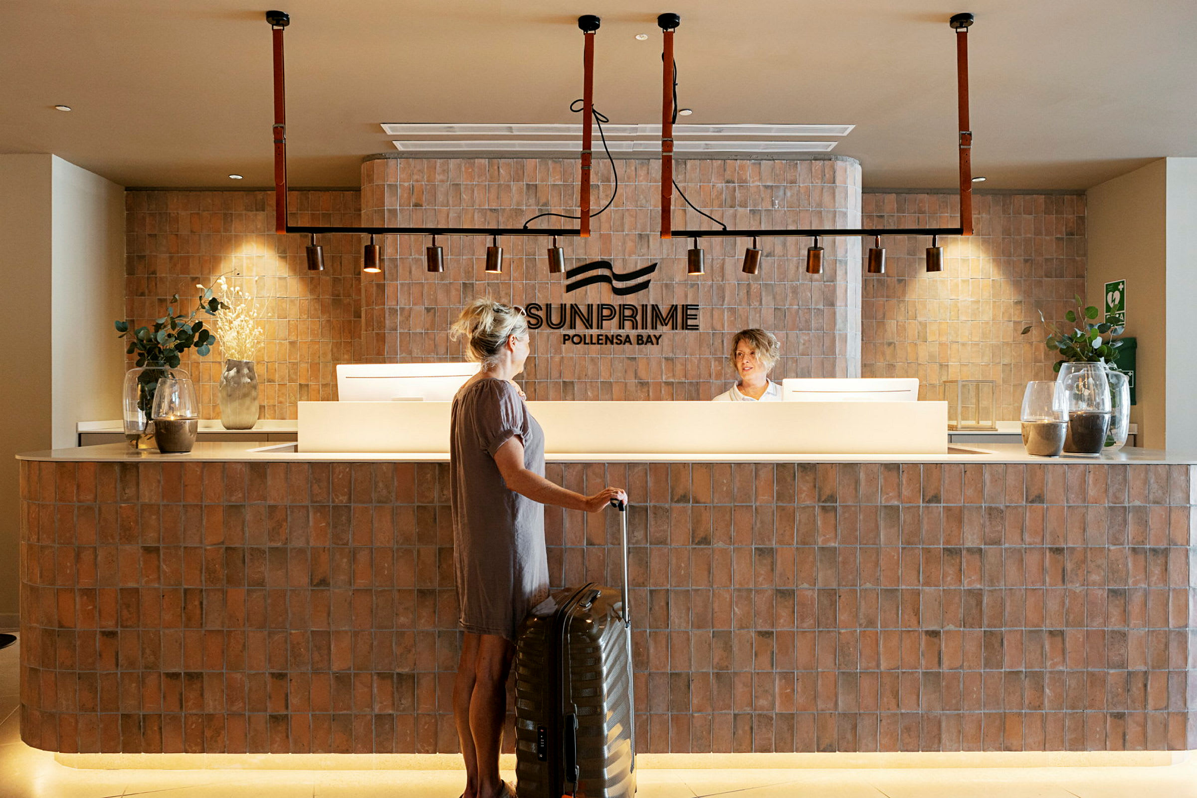 Receptionen på Sunprime Pollensa Bay med en person som står framför disken och en resväska. (AI-genererad text)
