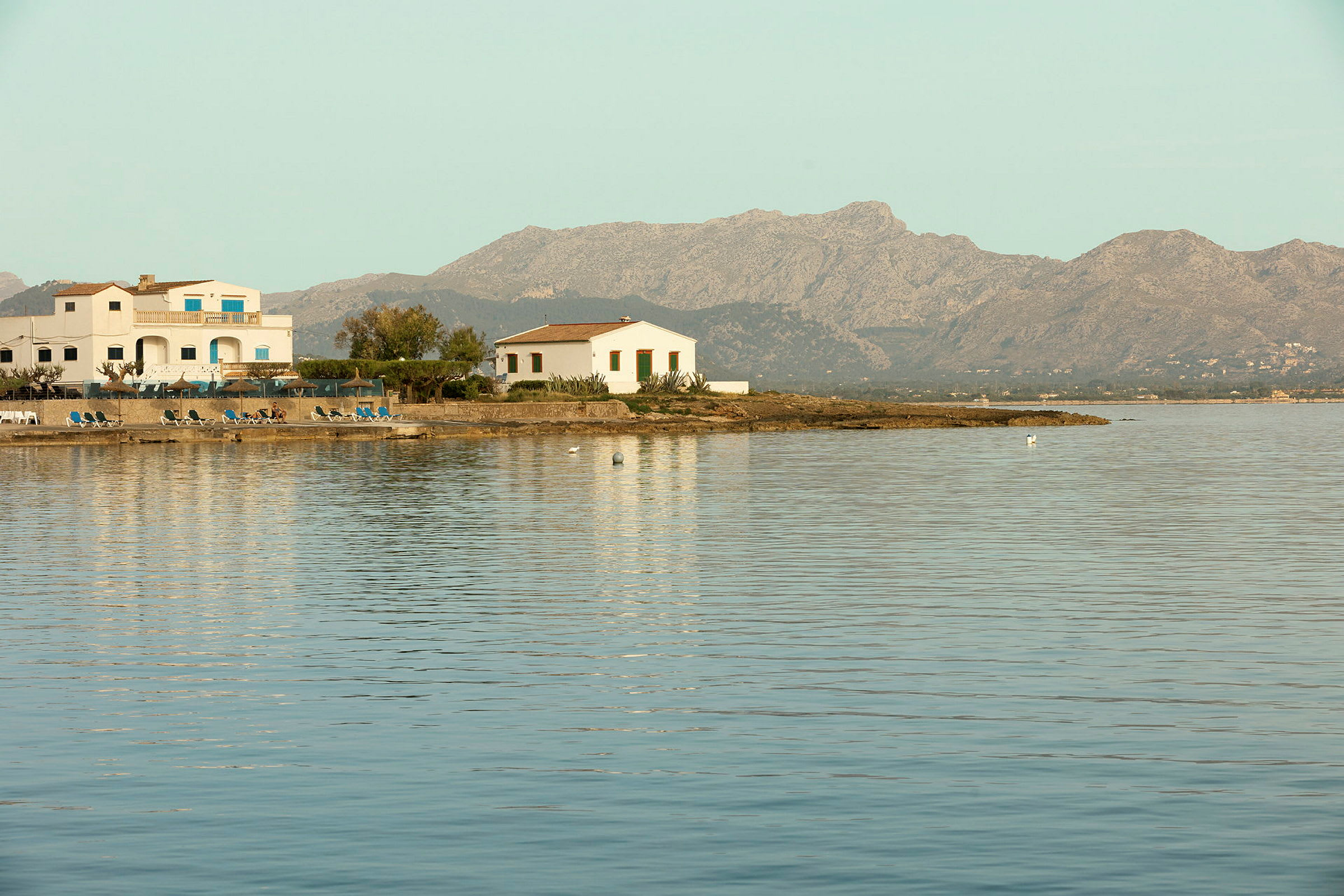 Flera hus vid en kust med berg i bakgrunden. (AI-genererad text)
