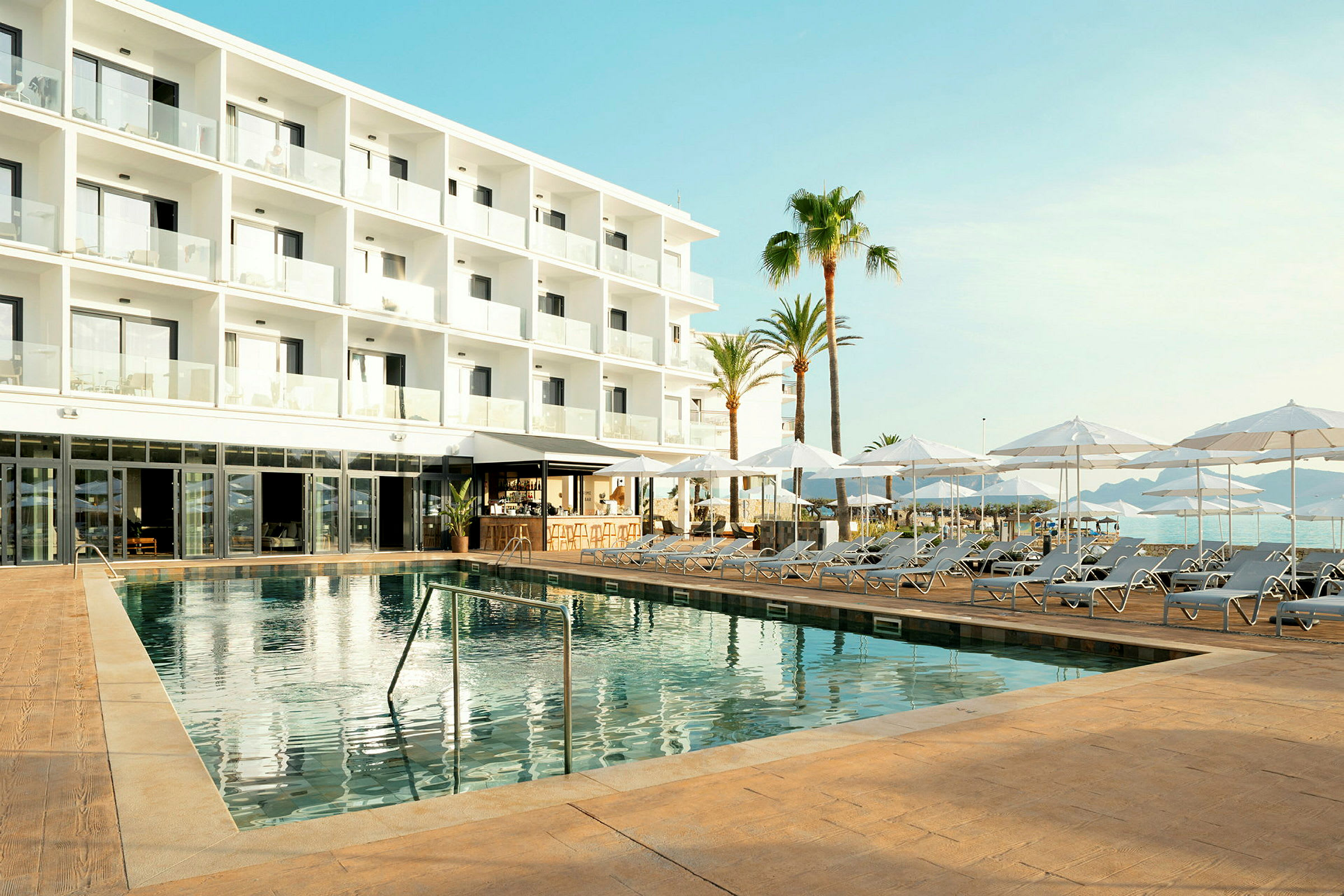 Modern hotellbyggnad med områden för solstolar och parasoller samt en swimmingpool. (AI-genererad text)