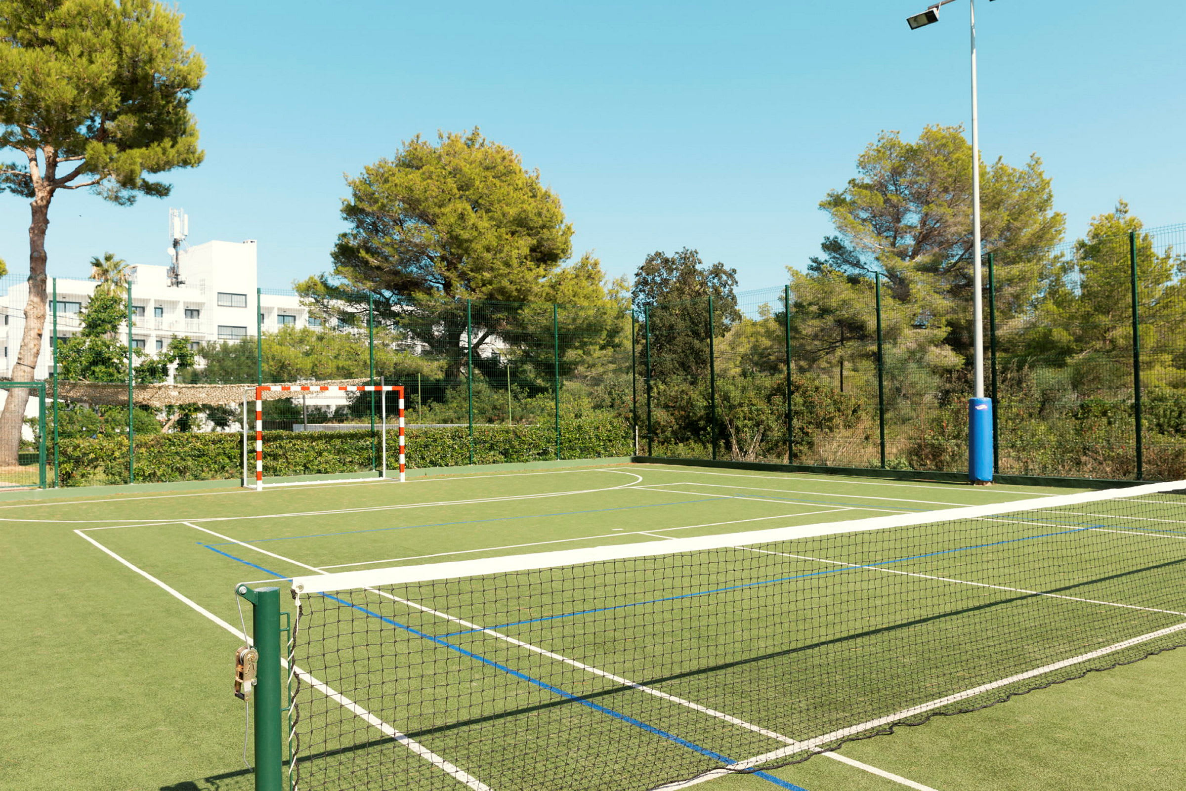 Upplyst sportplan med nät och målställning omgiven av grönska. (AI-genererad text)