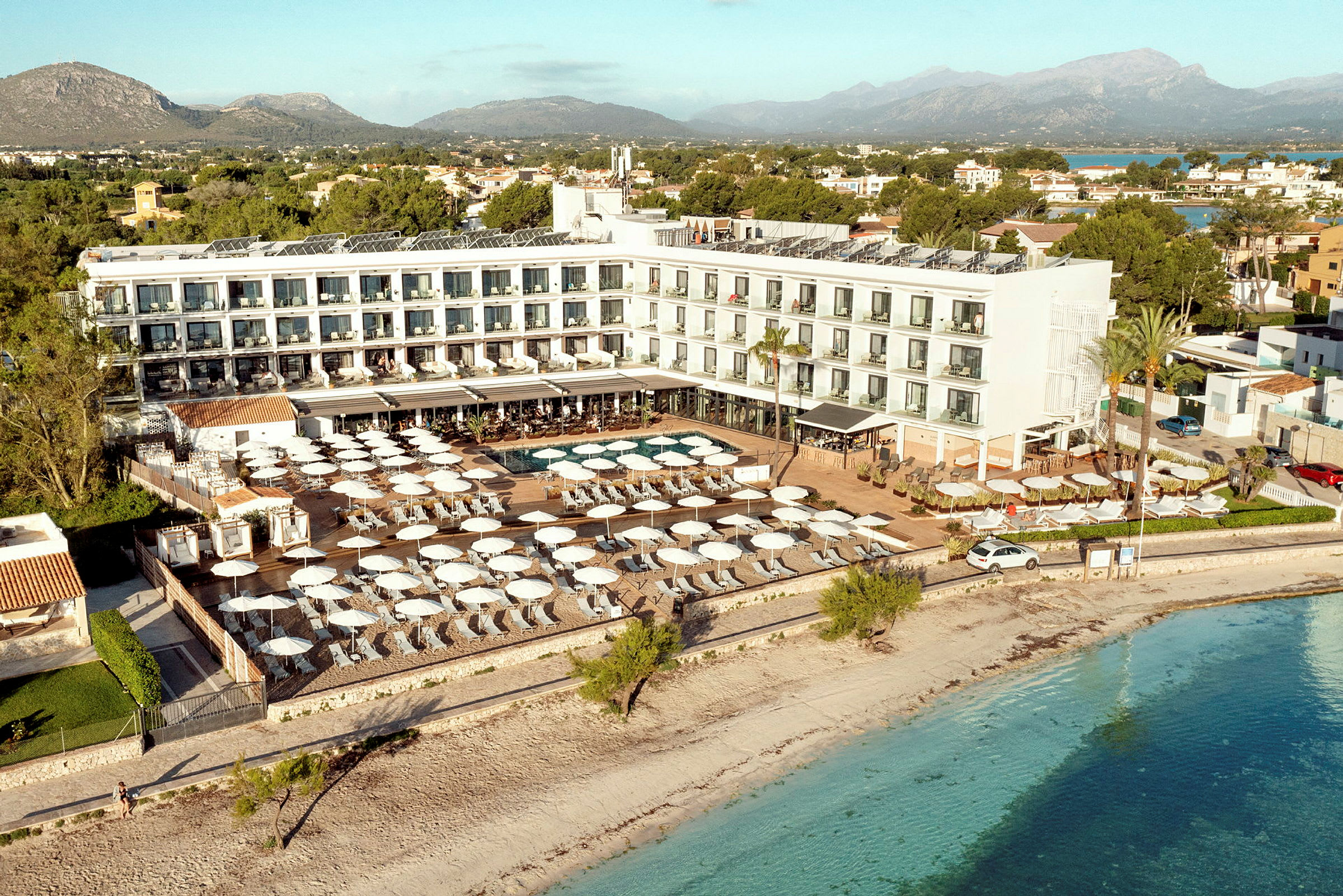 Flygbild av ett hotell vid stranden med poolområde och parasoller. (AI-genererad text)