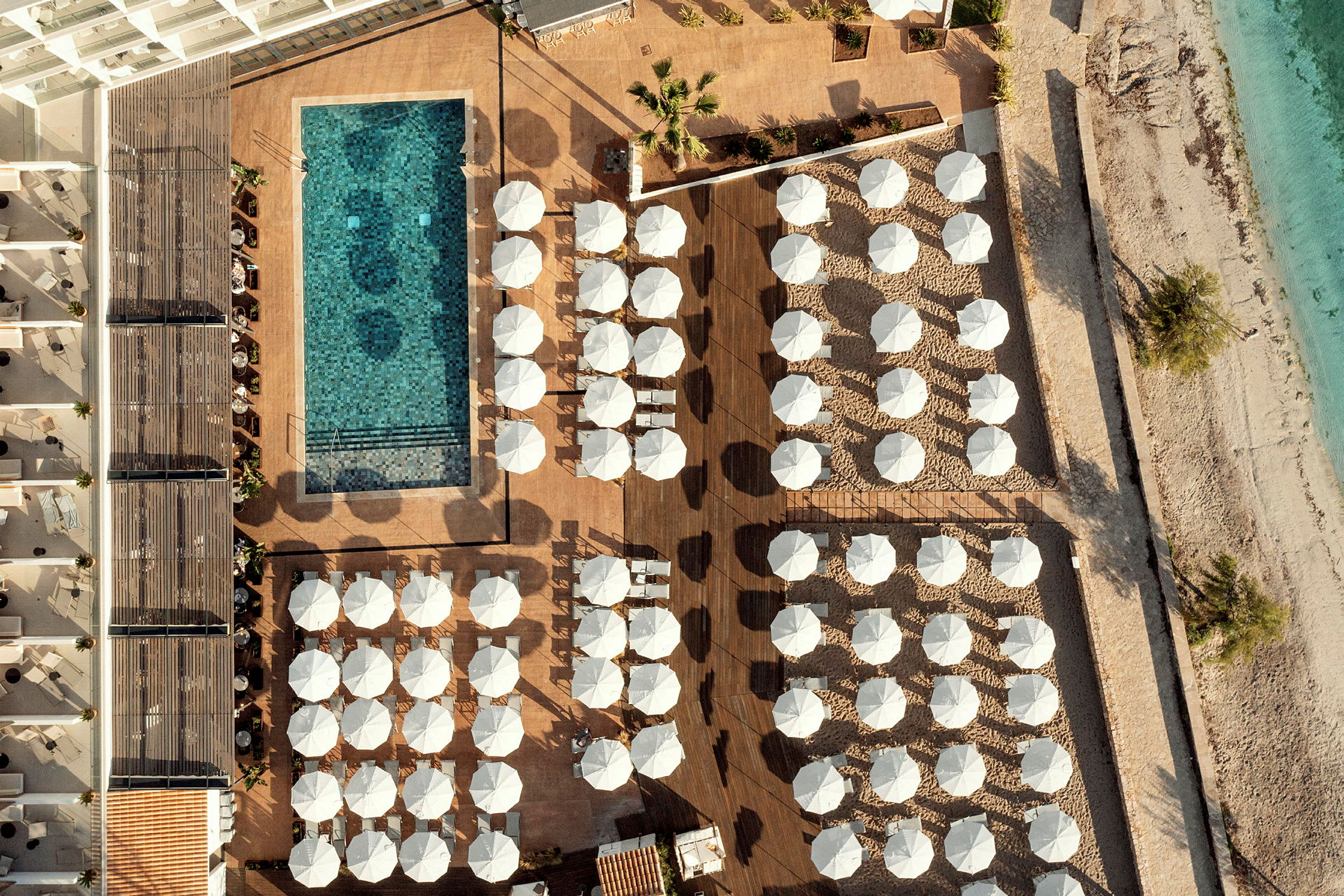 Flygfoto över en hotellpool omgiven av solstolar med parasoller, nära stranden. (AI-genererad text)