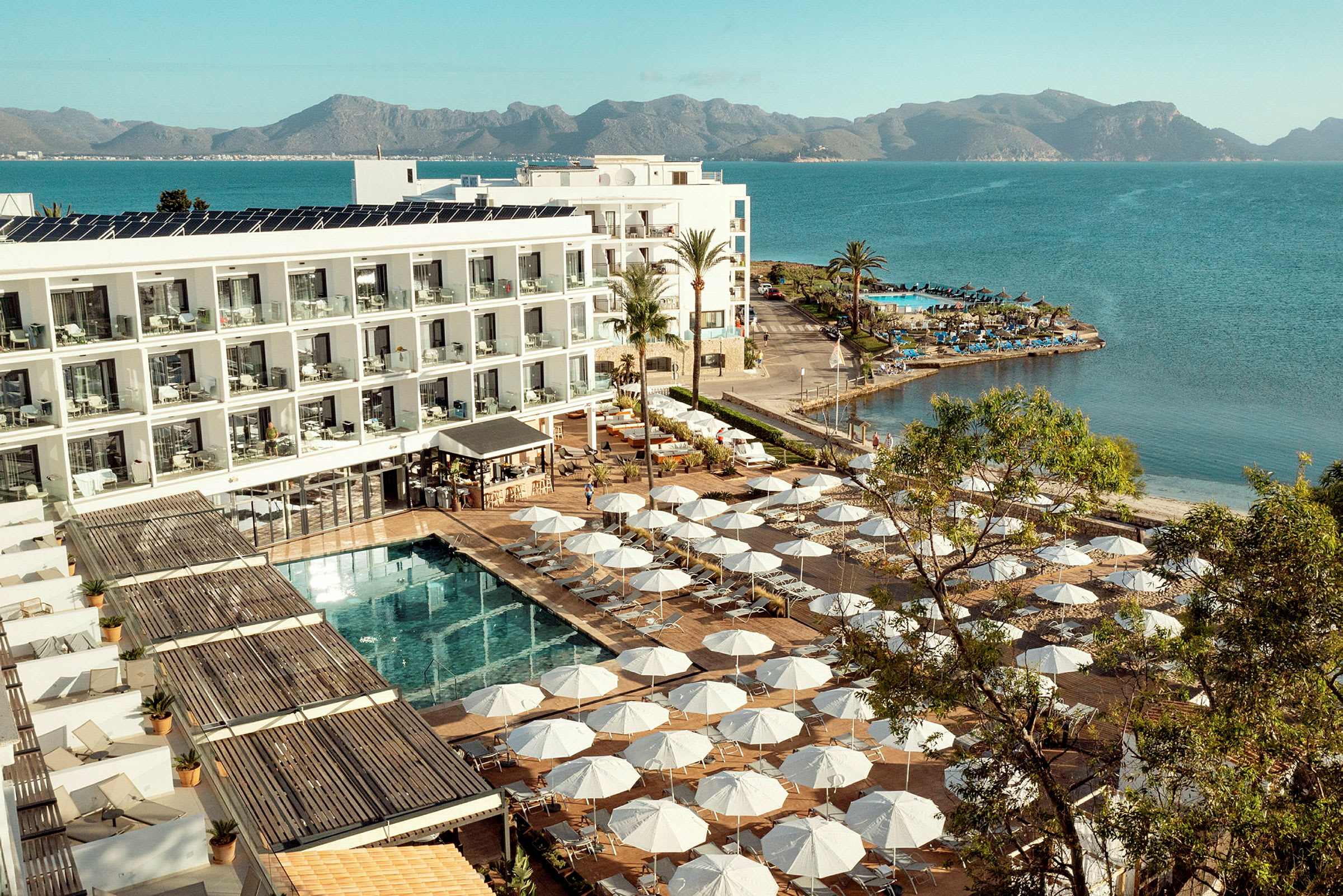 Hotellkomplex vid havskanten med solstolar och parasoller kring en pool. (AI-genererad text)