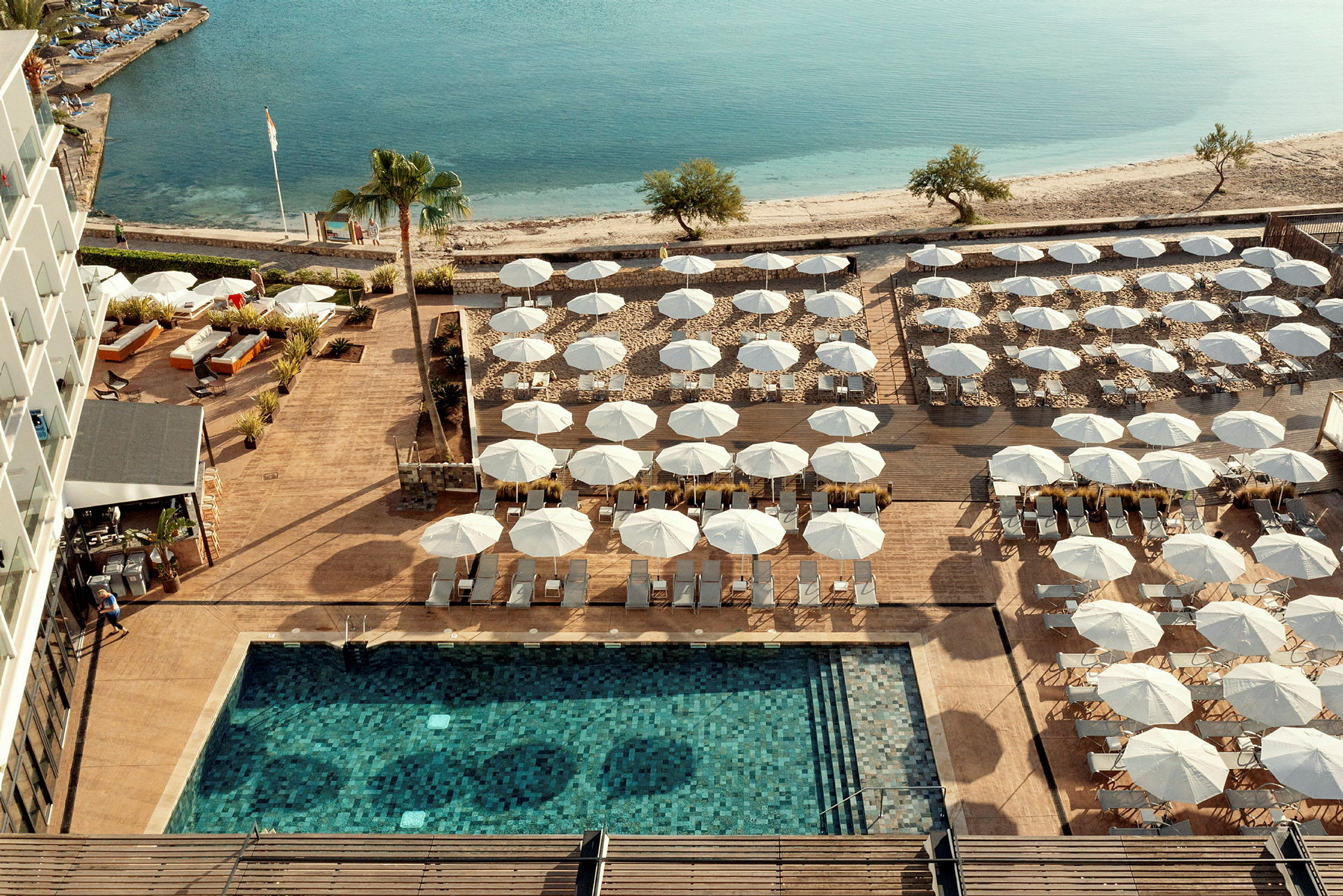 Vy över en pool, solstolar och parasoller bredvid stranden. (AI-genererad text)