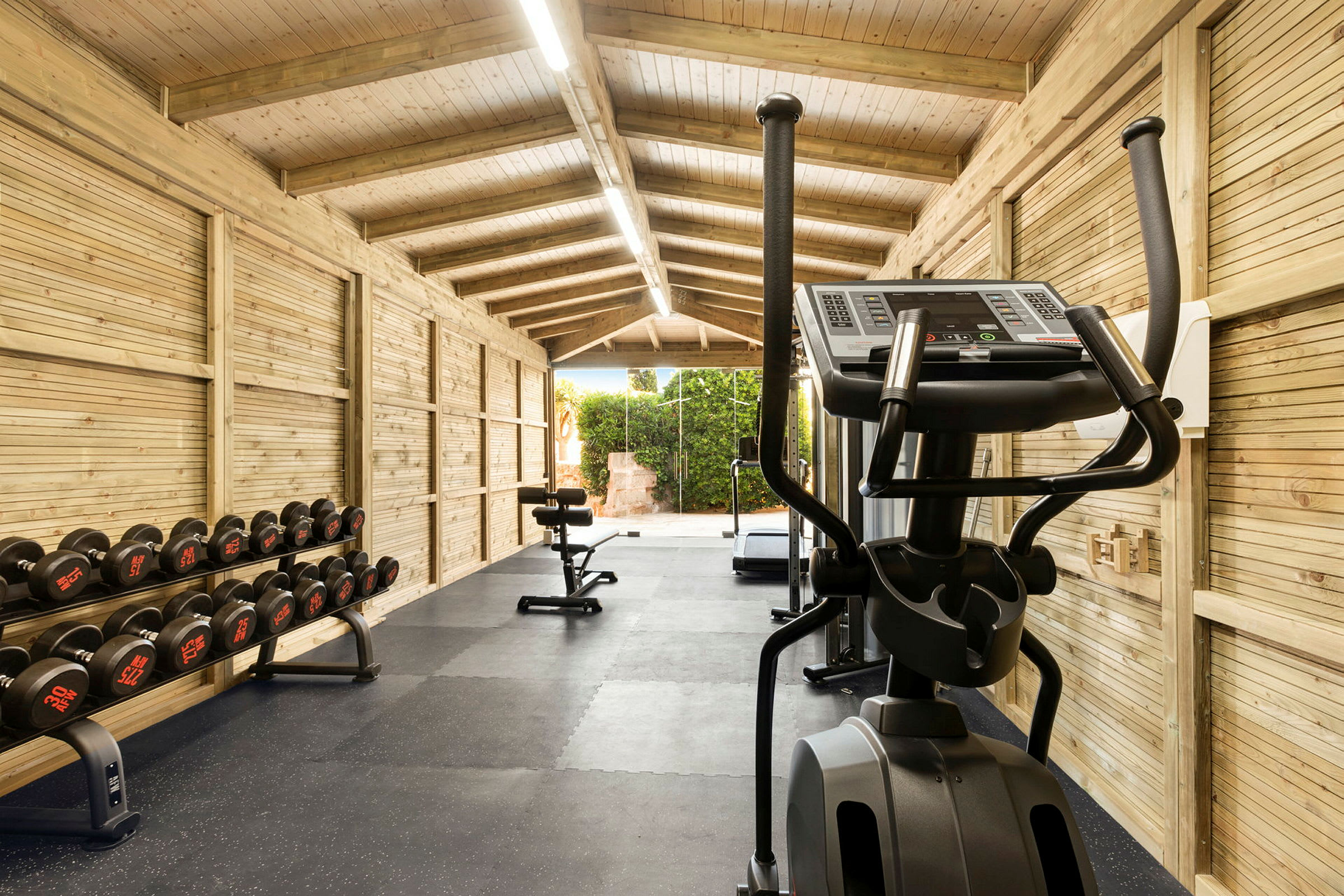 Ett gym med en löpband, hantlar och annan träningsutrustning i en ljus träbyggnad. (AI-genererad text)