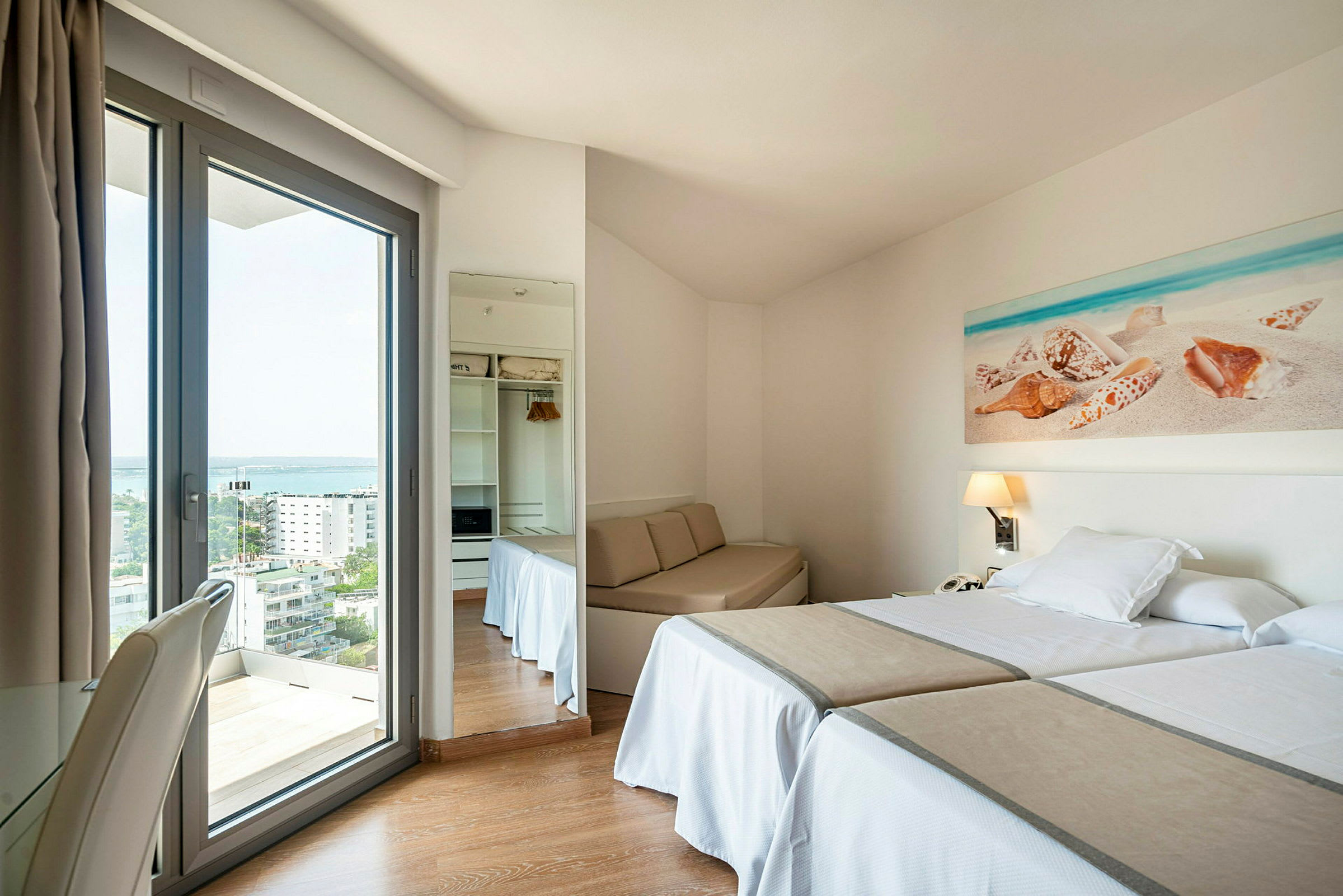 Ett hotellrum med två enkelsängar, ett litet bordställe och en glasdörr med utsikt utåt. (AI-genererad text)