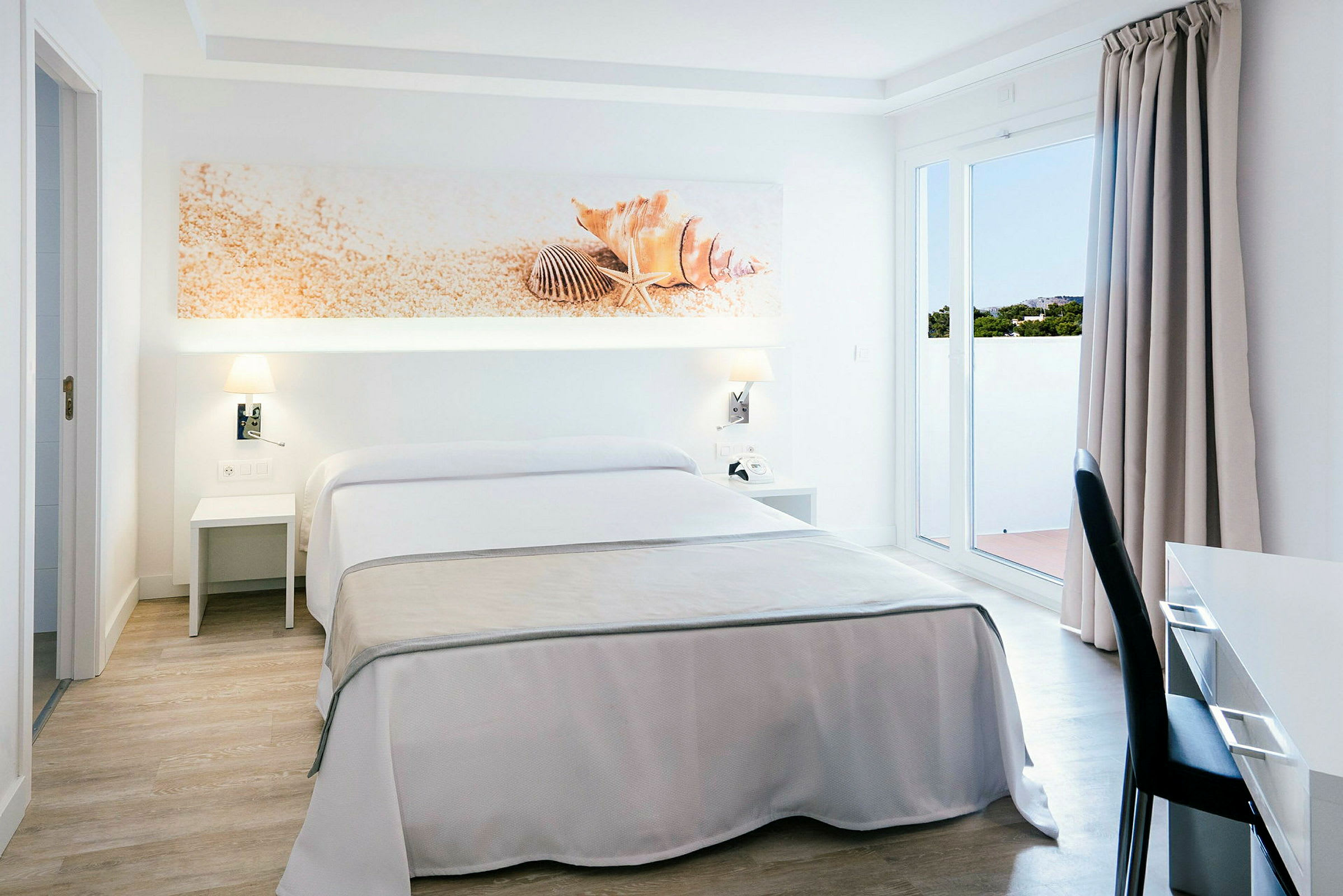 Ett hotellrum med dubbelsäng, vitt och beige inredning, dekoration med snäckskal ovanför sängen. (AI-genererad text)