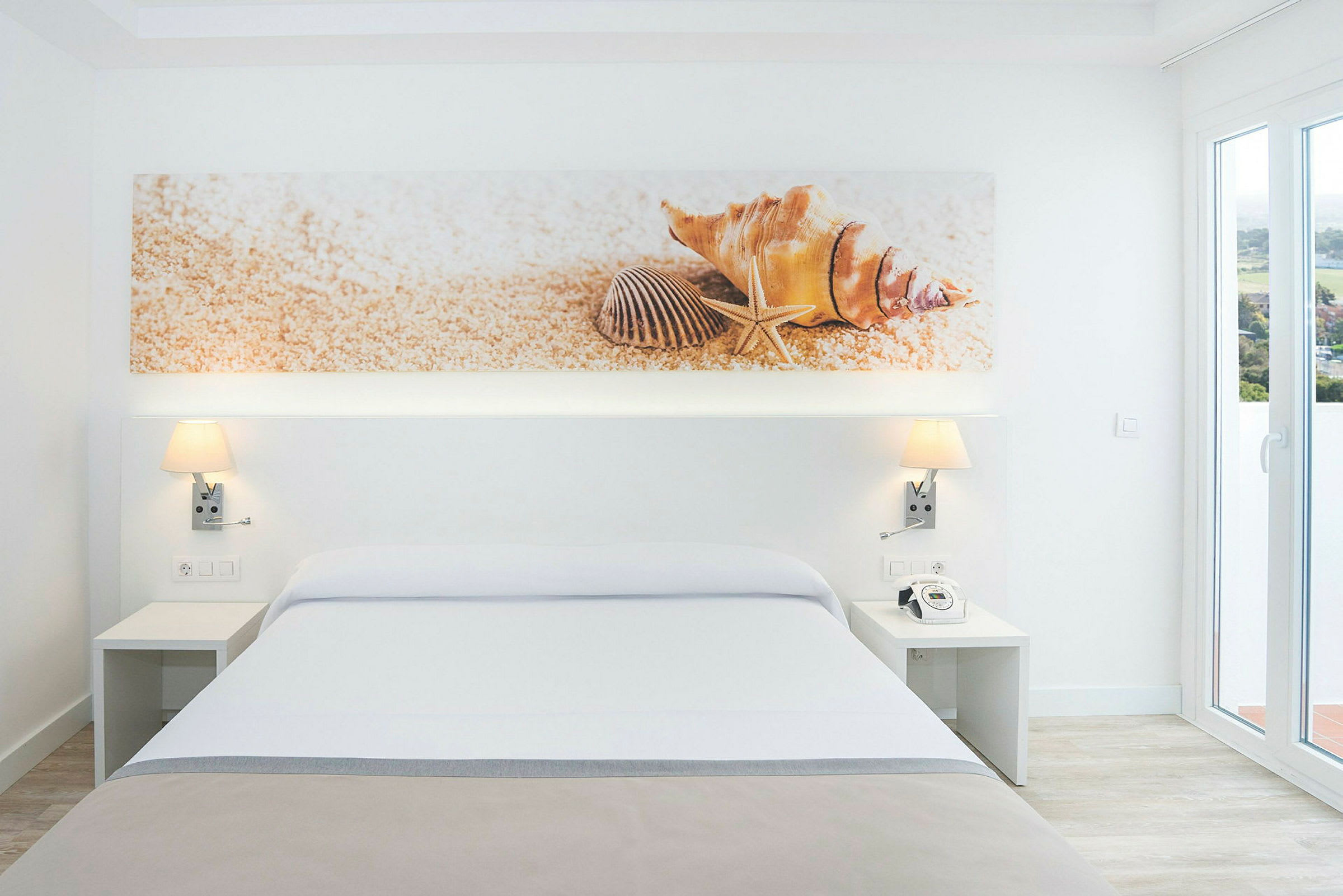 Modernt hotellrum med en stor säng och dekorativa tavla föreställandes snäckor ovanför. (AI-genererad text)