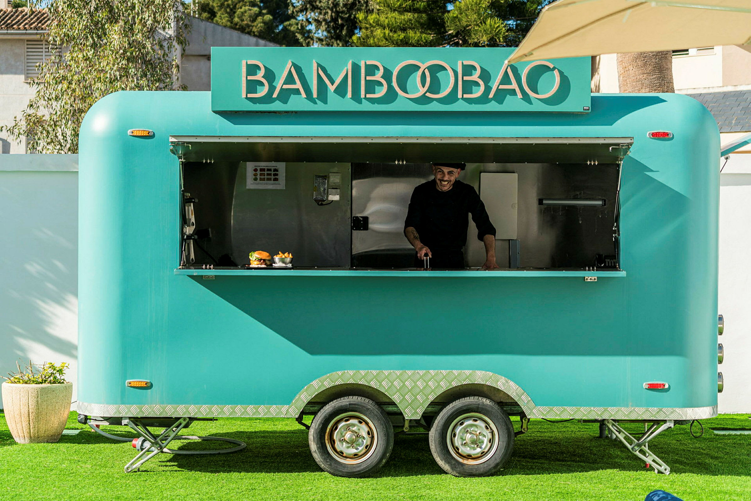 Turkos matvagn med texten 'Bamboobao' på framsidan, står på gräs med öppet serveringsfönster. (AI-genererad text)