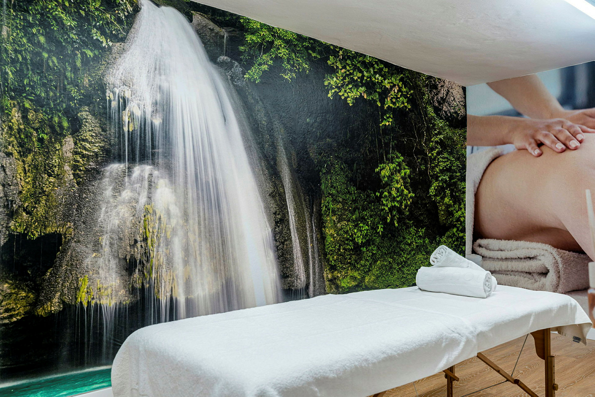 Massagebänk framför en vägg med bildmotiv av ett vattenfall. (AI-genererad text)