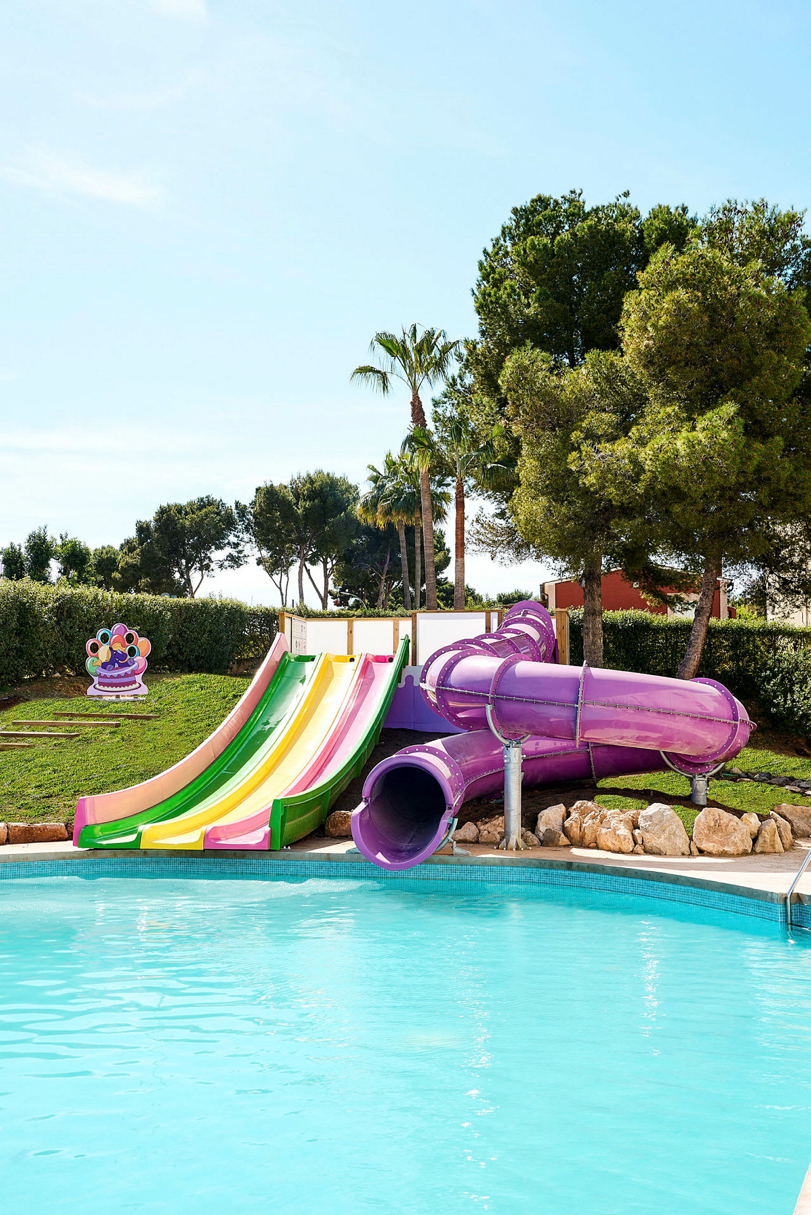 Bild av en pool med färgglada vattenrutschbanor och träd i bakgrunden. (AI-genererad text)