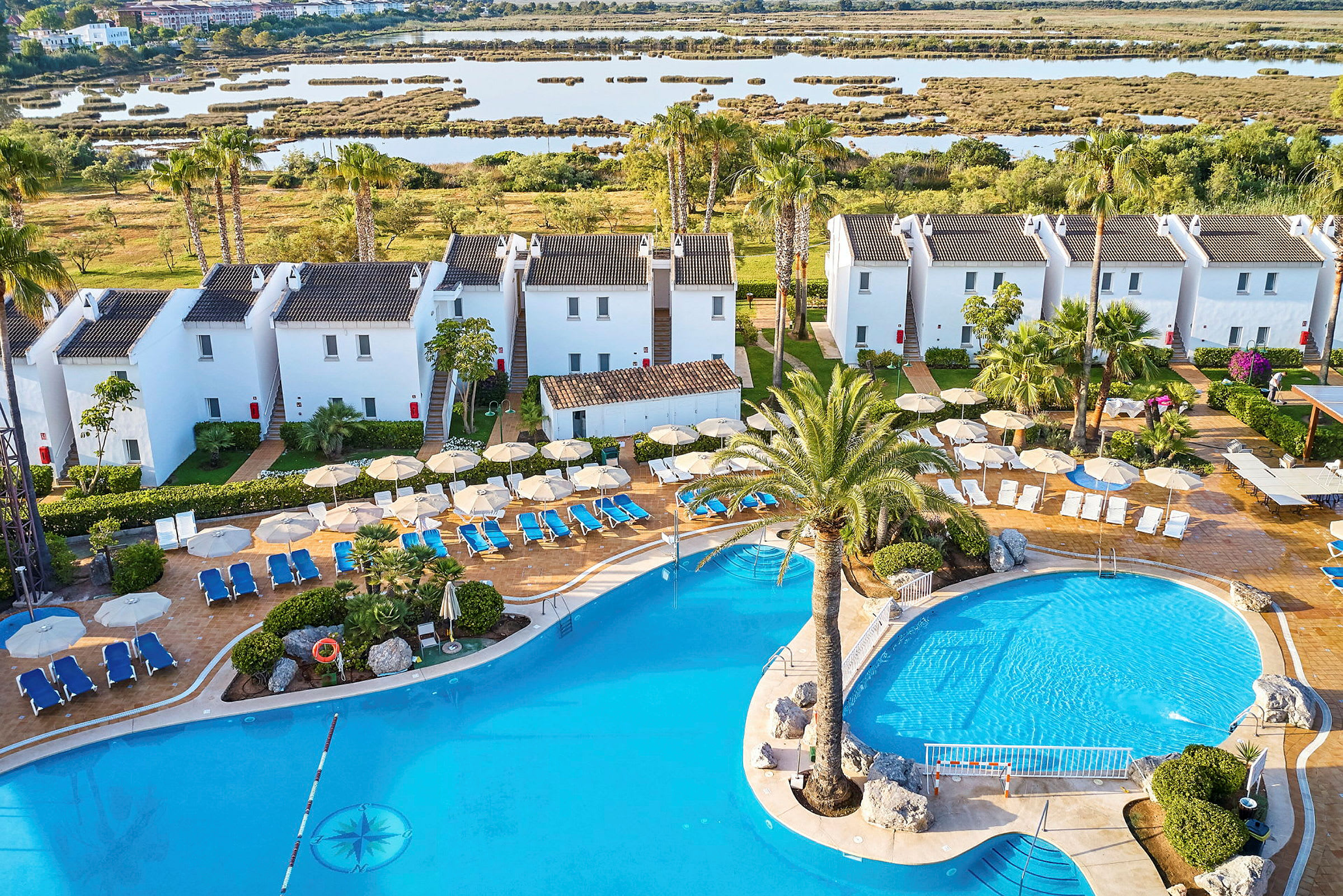 En vy över ett hotellområde med vita byggnader, en pool och omgivande vegetation. (AI-genererad text)
