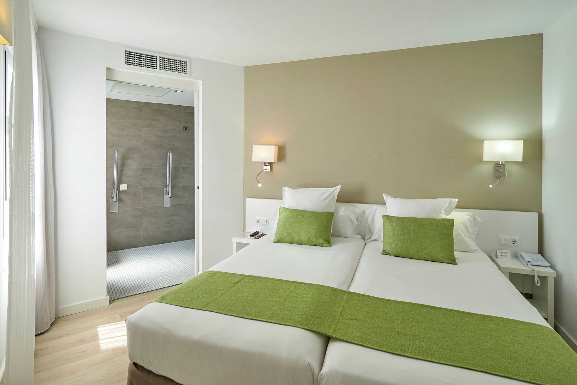 Hotellrum med två enkelsängar, gröna sängkläder och en öppning mot badrummet. (AI-genererad text)