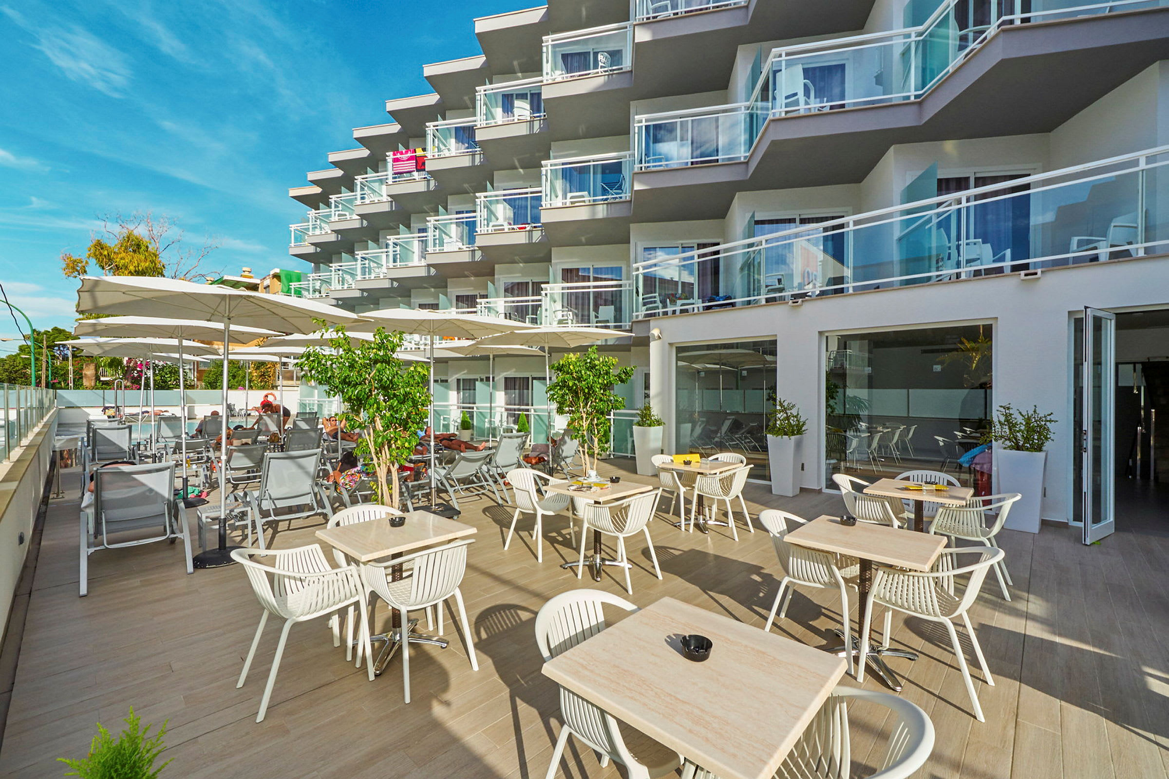 Utomhusområde med bord och stolar samt solstolar vid ett hotell med balkonger. (AI-genererad text)