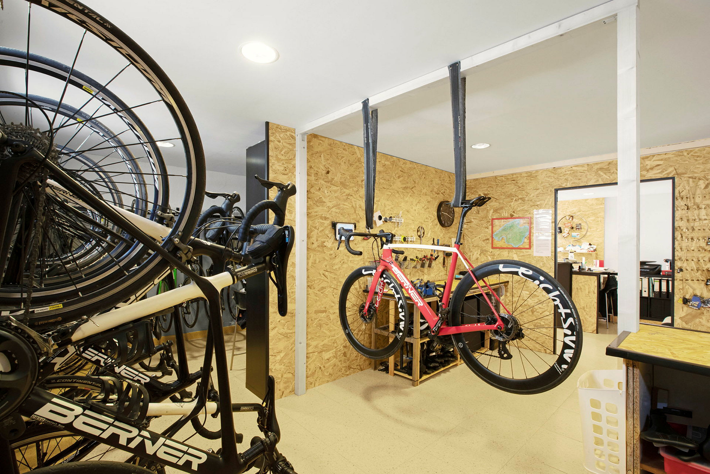 Ett verkstadsrum med cyklar och en upphängd röd vägcykel. (AI-genererad text)