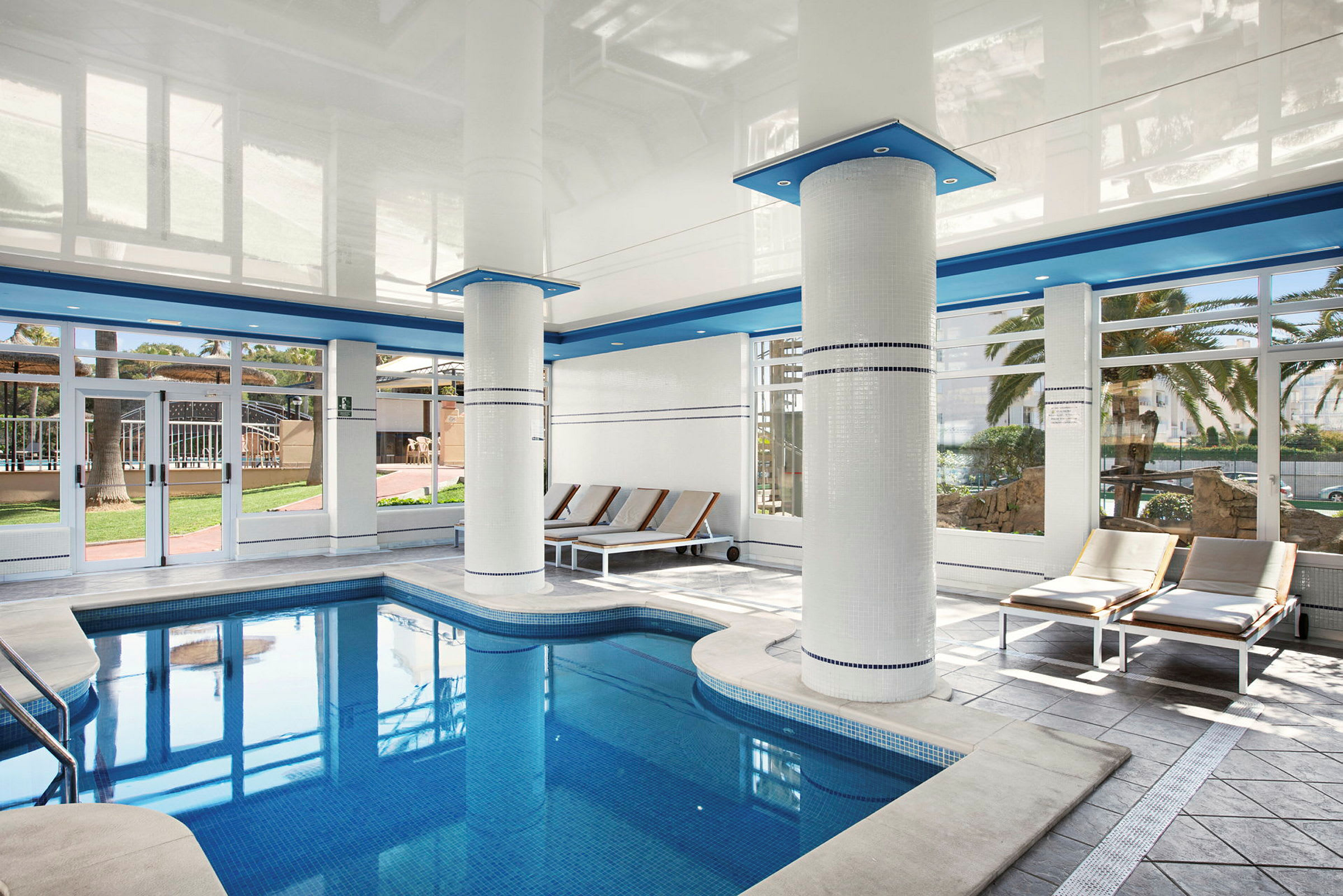 Inomhuspool med solstolar och stora fönster. (AI-genererad text)