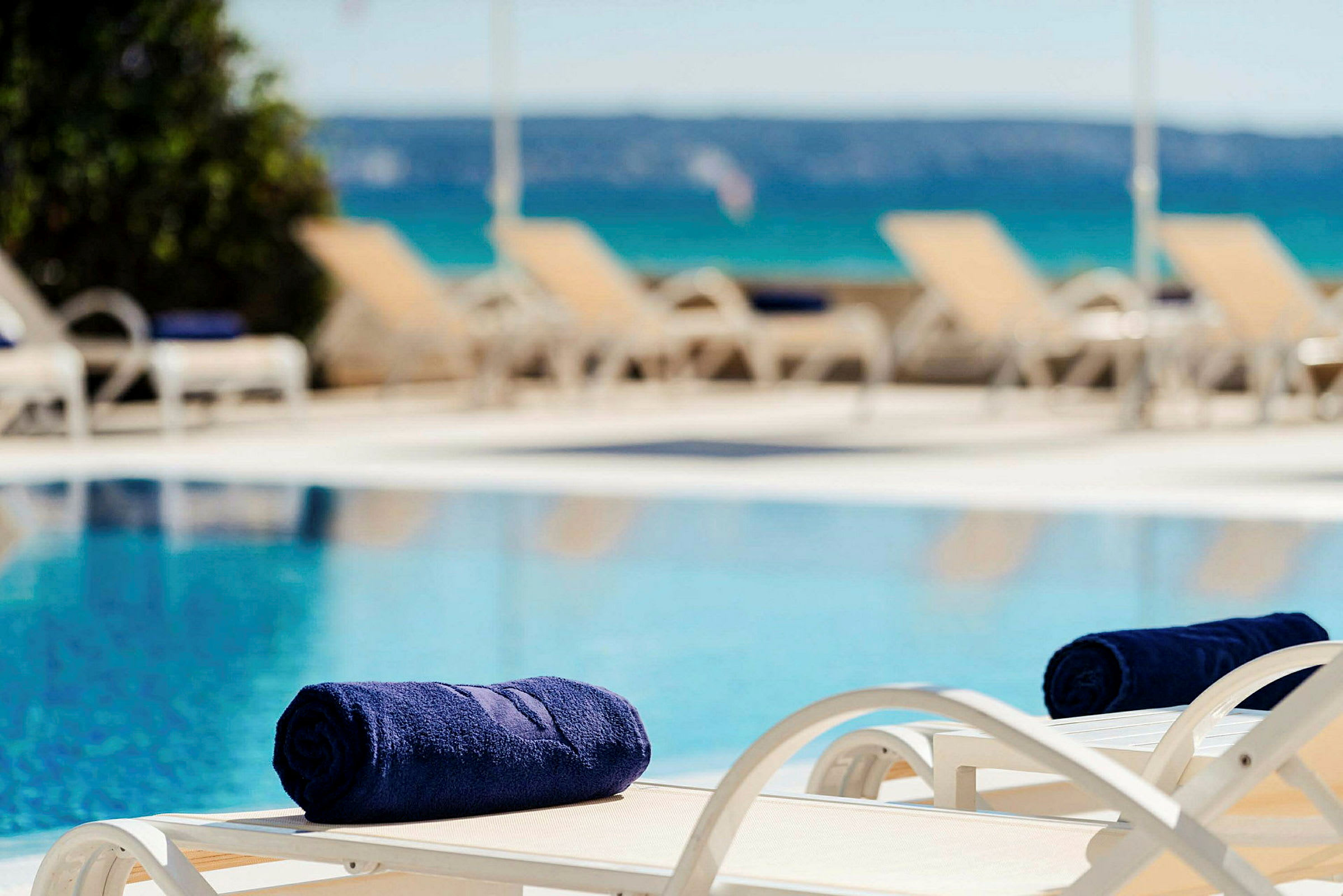 Utsikt över en pool där solstolar och handdukar är placerade nära vattnet. (AI-genererad text)