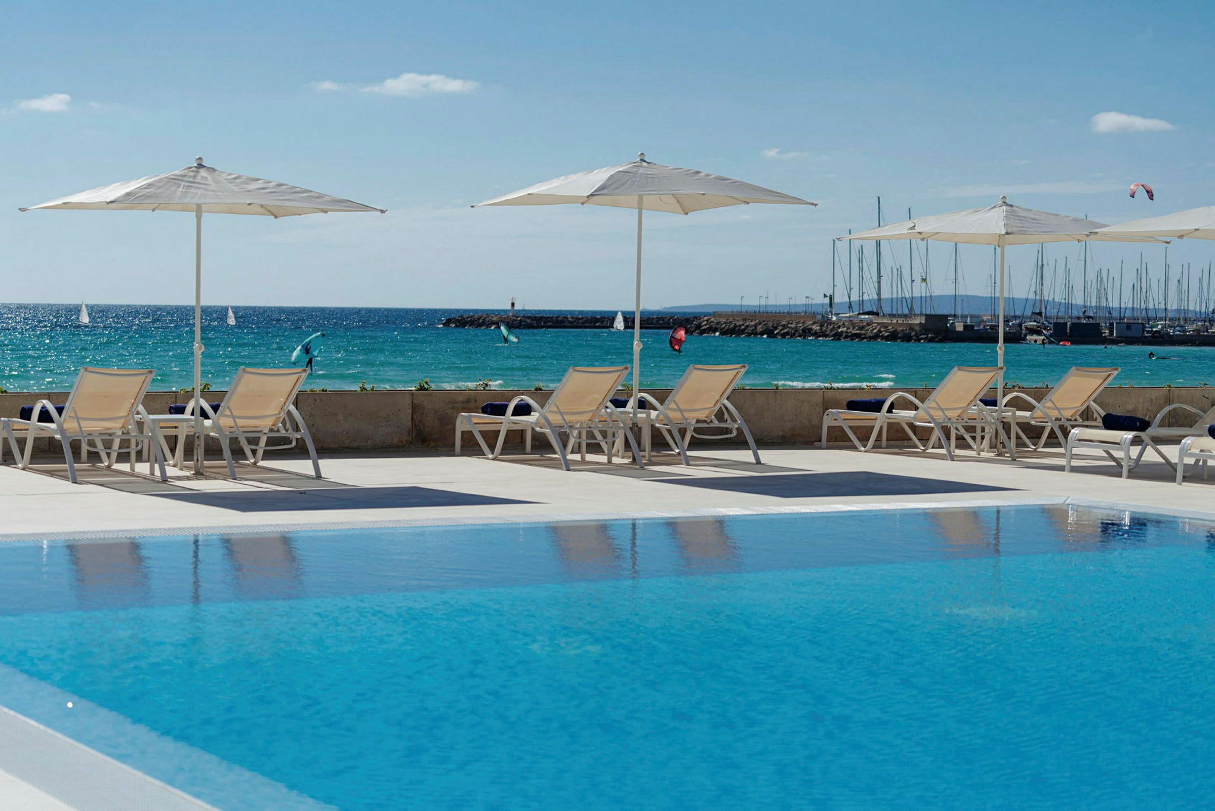 Solstolar och parasoller vid en pool med utsikt över havet och en marina i bakgrunden. (AI-genererad text)
