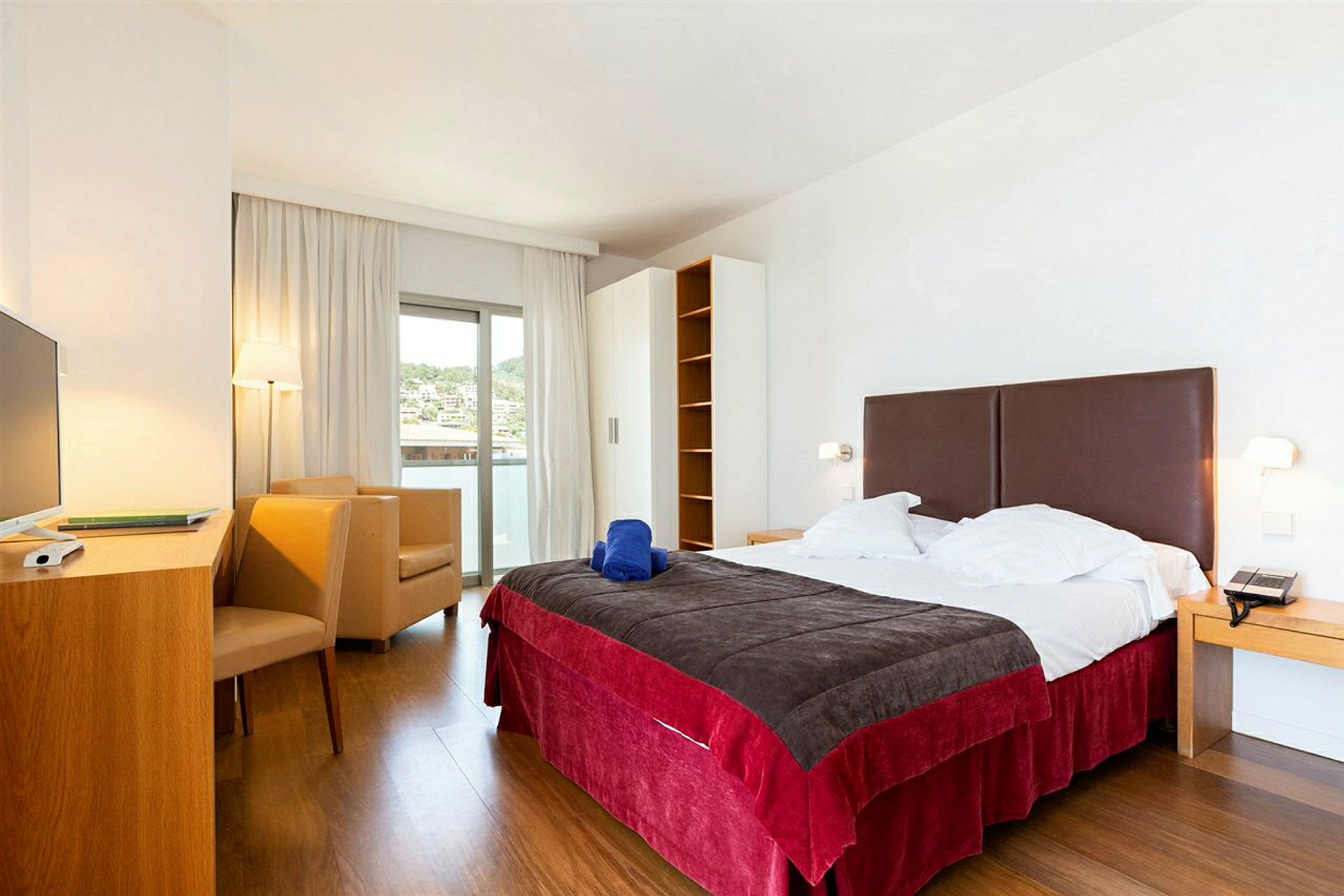 Ett hotellrum med en stor säng, en skrivbordshörna och en sittgrupp nära en balkongdörr. (AI-genererad text)