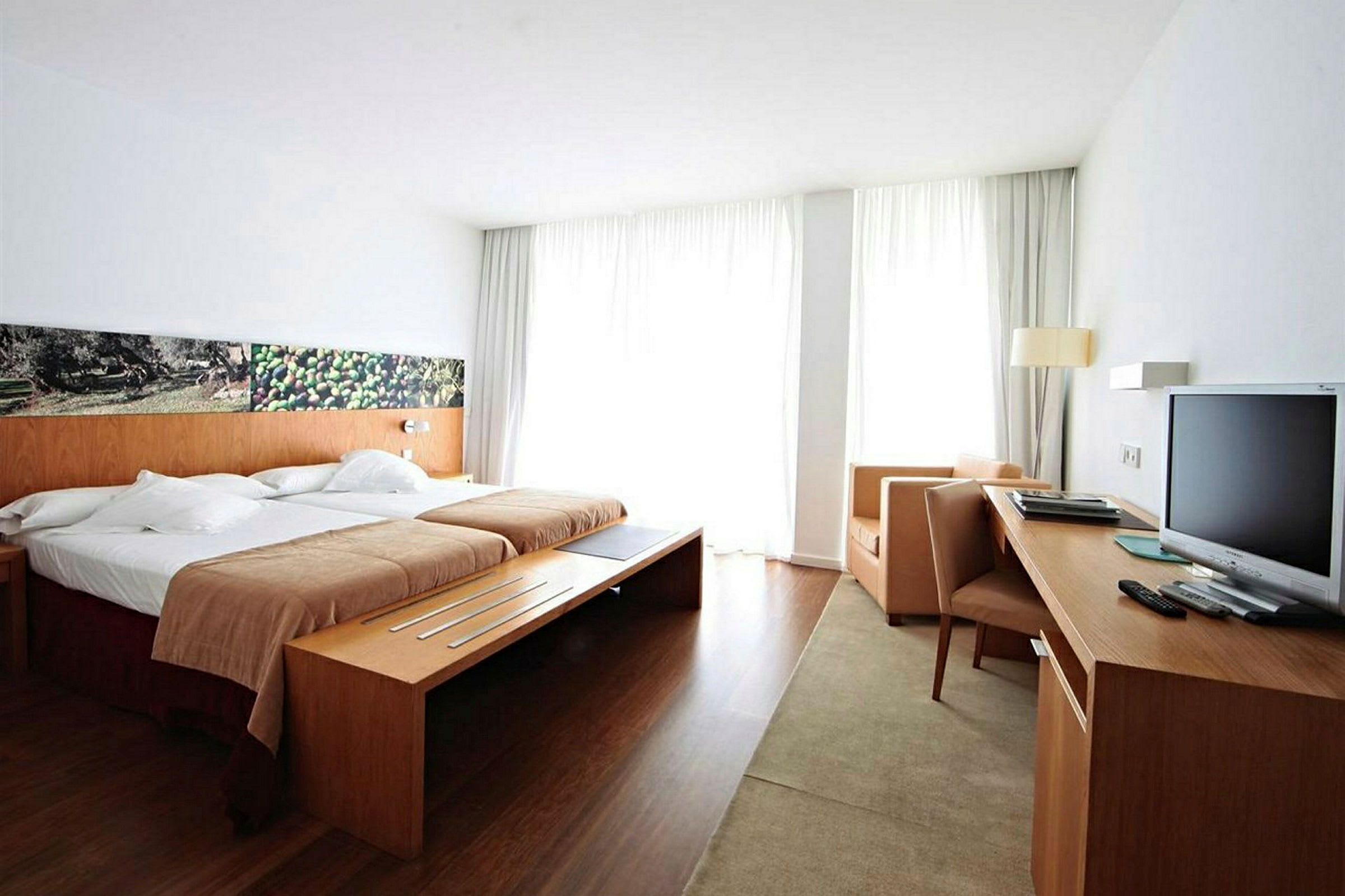Ett hotellrum med en dubbelsäng, skrivbord, tv och stolar. (AI-genererad text)