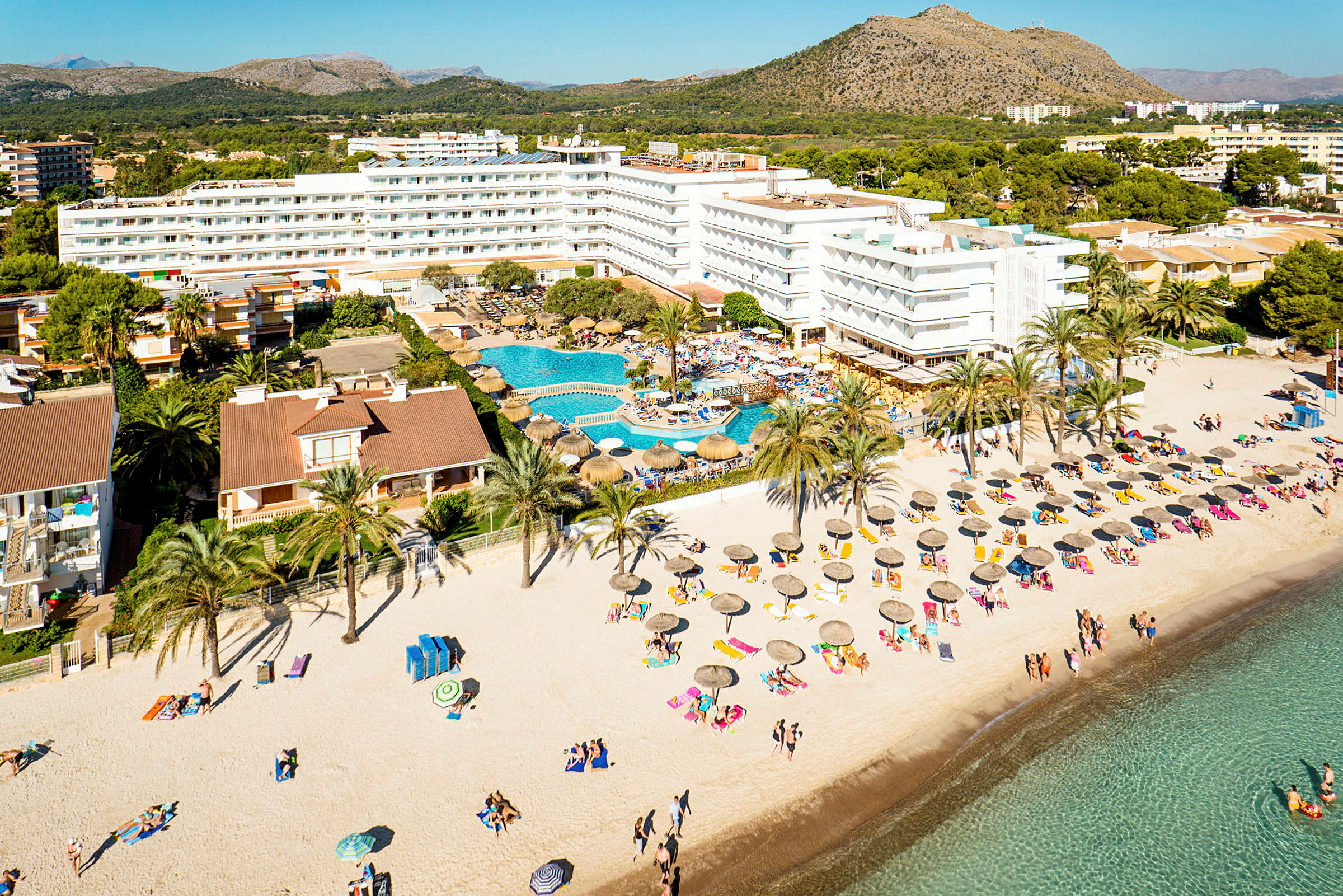 Flygvy över ett strandhotell med pool och parasoller på sanden. (AI-genererad text)