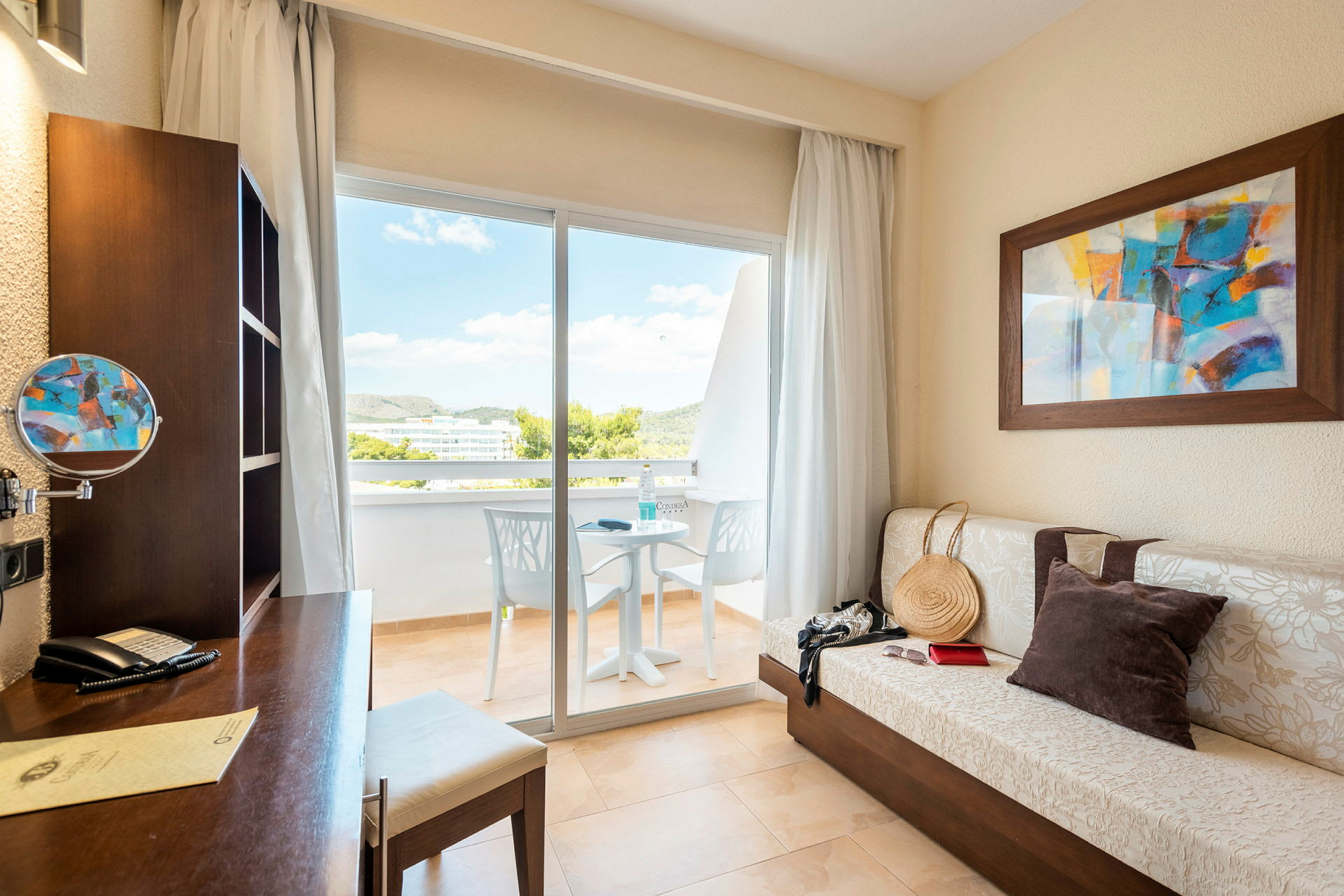 Ett hotellrum med skrivbord, soffa, tavla och utgång till balkong. (AI-genererad text)