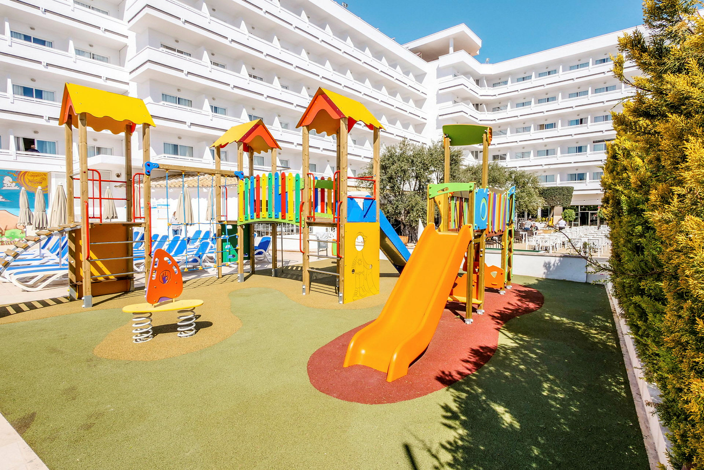 Lekplats med klätterställning och rutschkana framför ett hotell. (AI-genererad text)