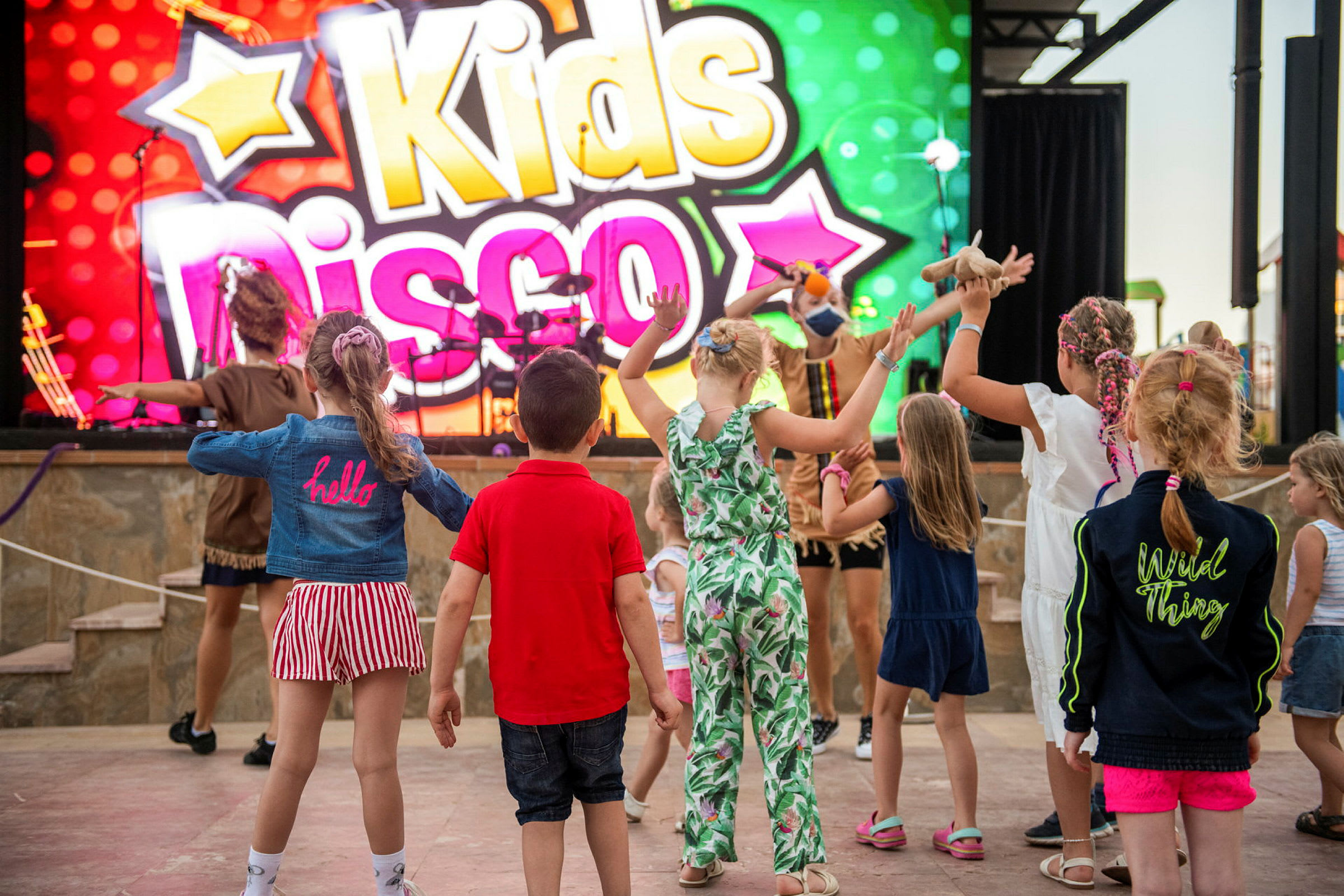 Barn som dansar framför en färgglad skylt med texten 'Kids Disco'. (AI-genererad text)