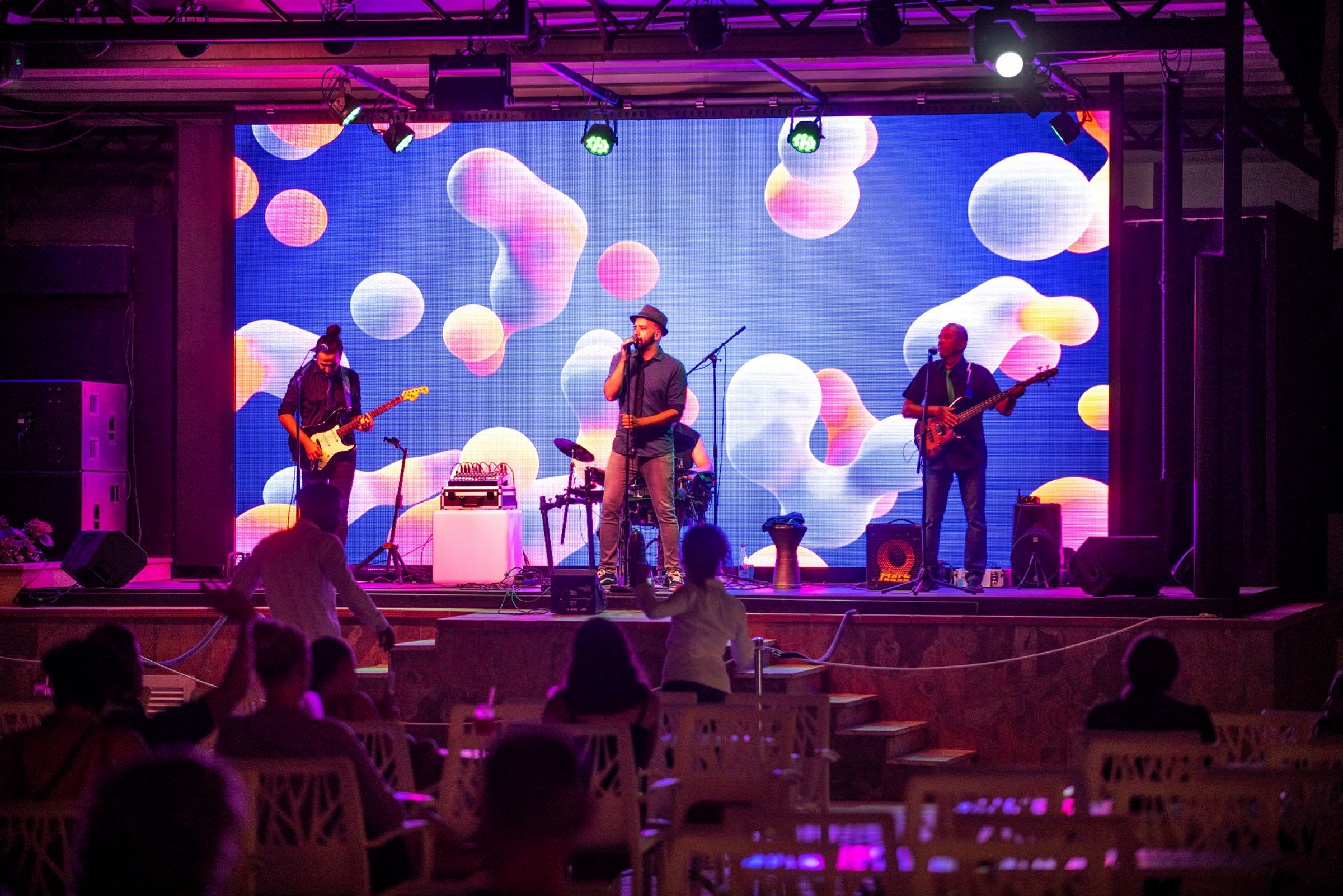 En musikkonsert med ett band på scen och en färgglad bakgrund. (AI-genererad text)