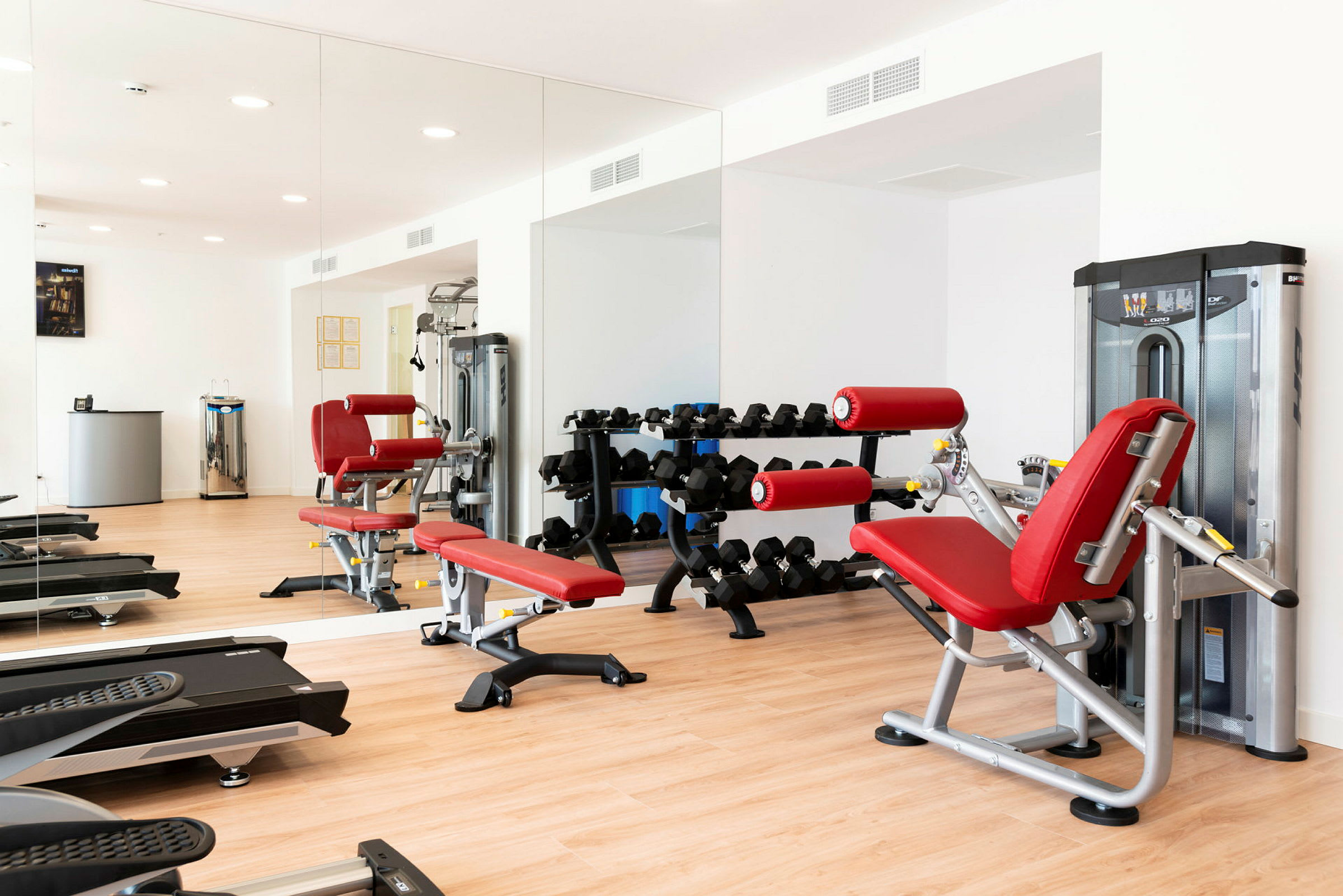 Bild av ett gym med träningsutrustning, röd bänk och spegelvägg. (AI-genererad text)