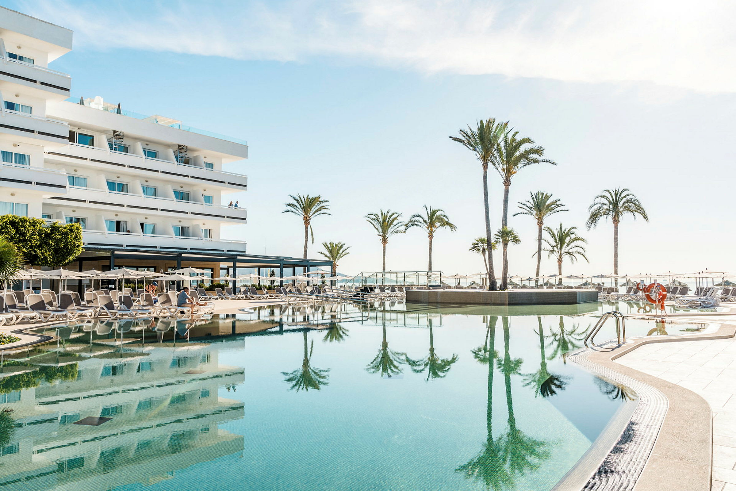 Hotell med swimmingpool och solstolar vid en solig strand. (AI-genererad text)