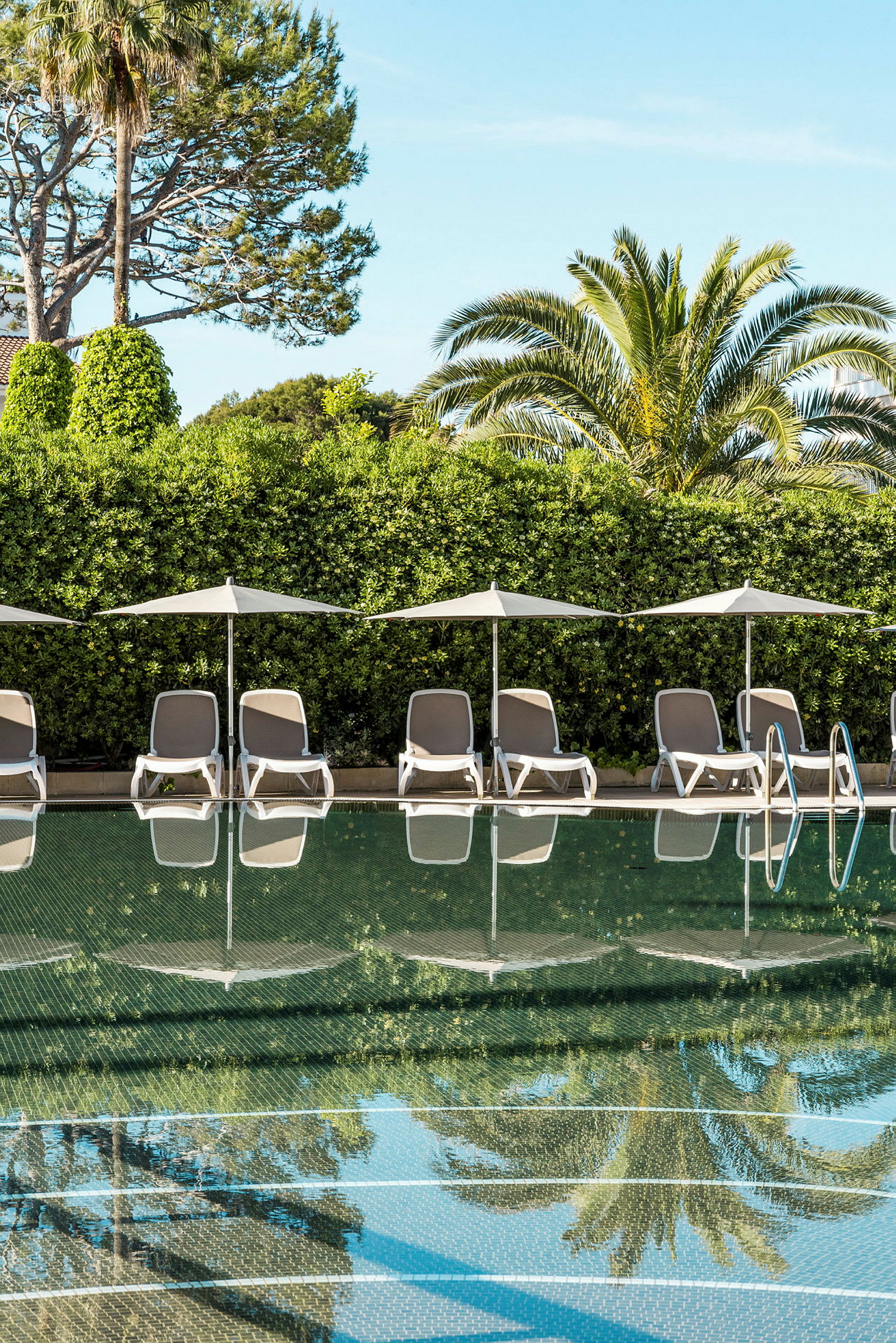 Bild på en pool med solstolar och parasoll vid kanten, omgiven av grönska. (AI-genererad text)