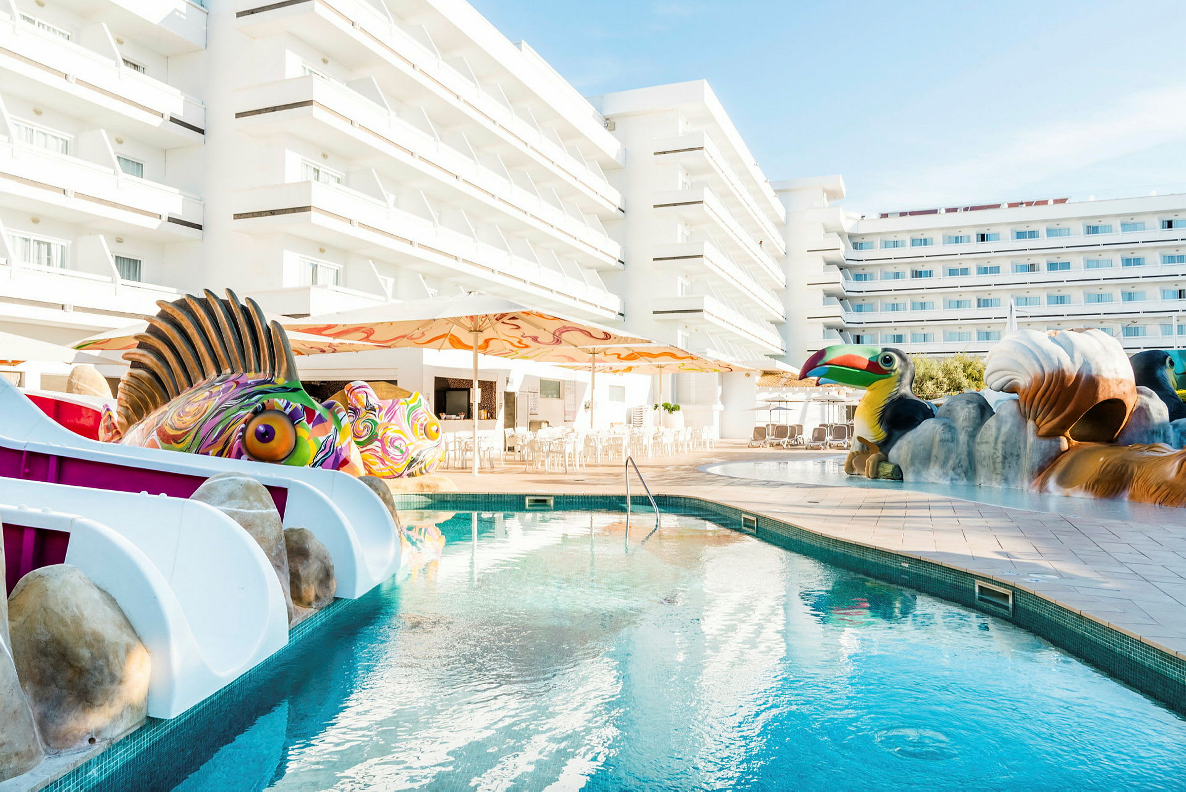 En pool med leksakssjöjungfrur och faunafigurer framför hotellbyggnader. (AI-genererad text)