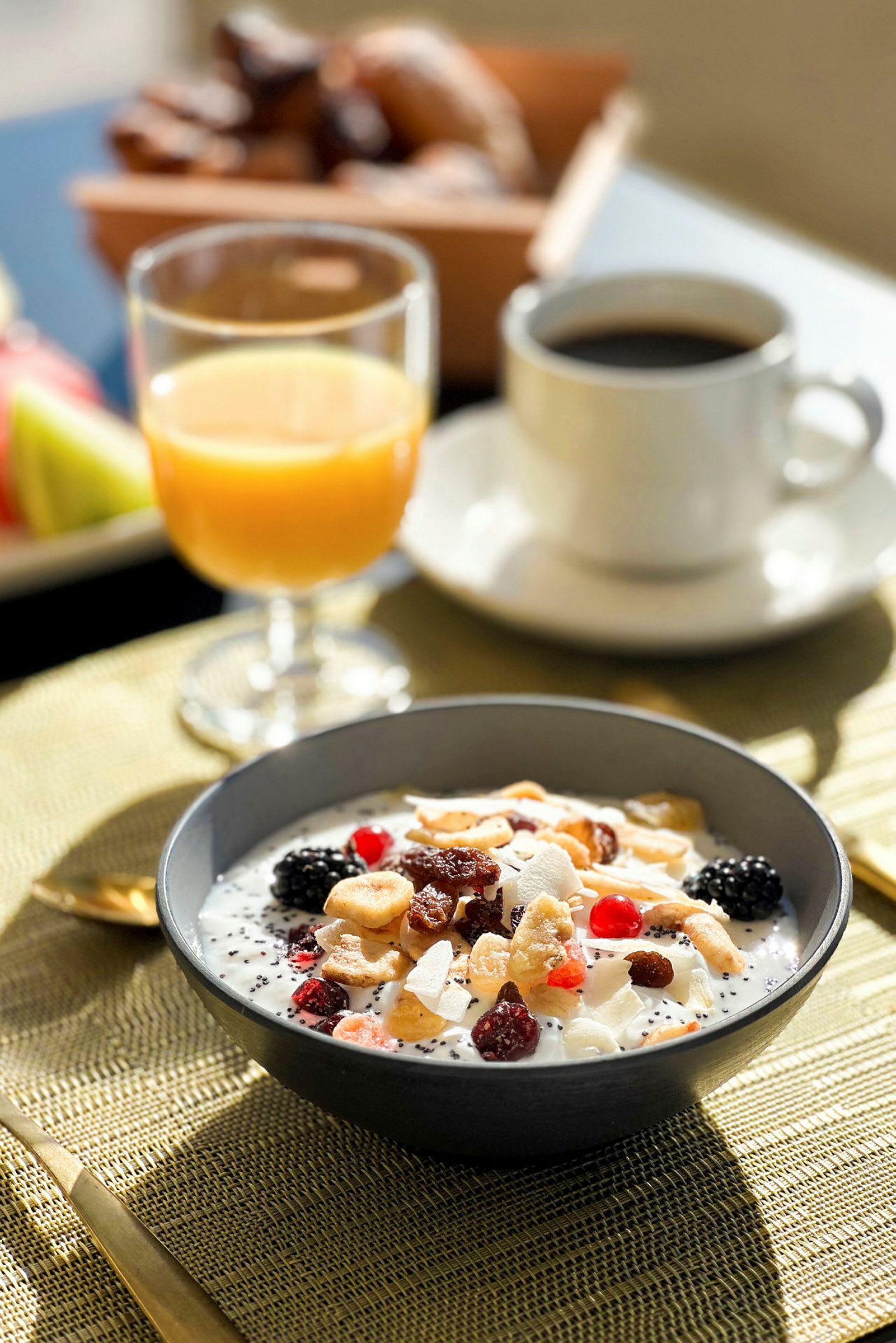 En frukostskål med yoghurt, frukt och nötter bredvid ett glas apelsinjuice och en kopp kaffe. (AI-genererad text)