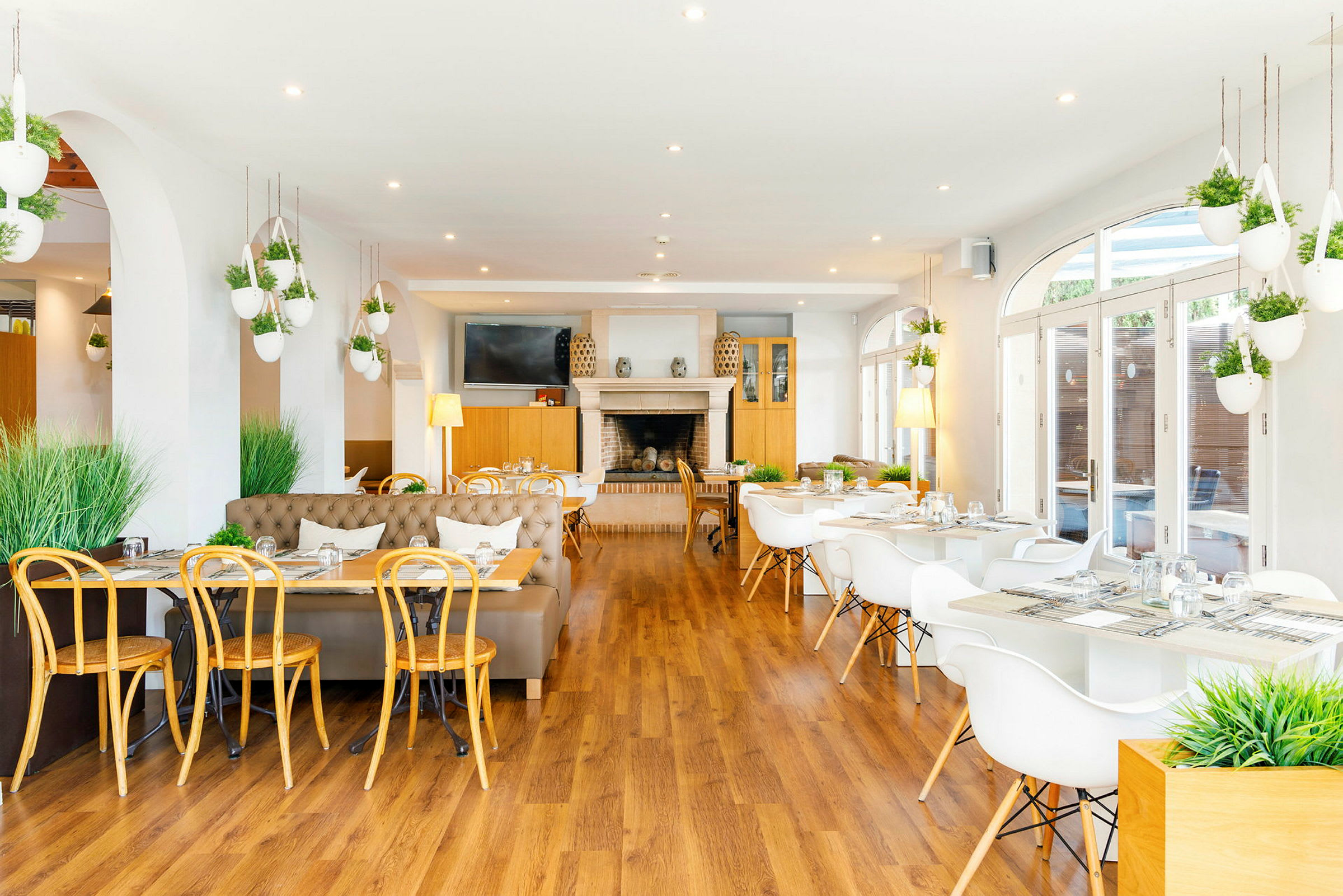 En ljus restaurang med moderna möbler och vita bord omgivna av gröna växter. (AI-genererad text)