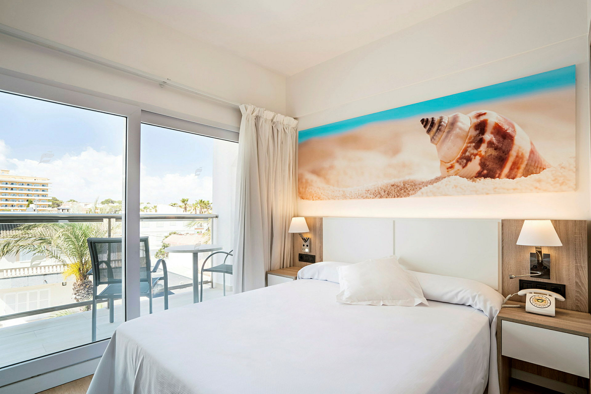 Hotellrum med balkong och utsikt, säng och dekoration av strandmotiv. (AI-genererad text)