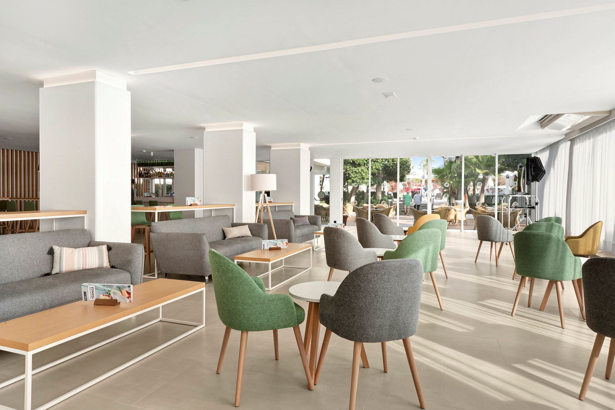 En ljus och modern lounge med gröna och gråa stolar, bord och stora fönster. (AI-genererad text)