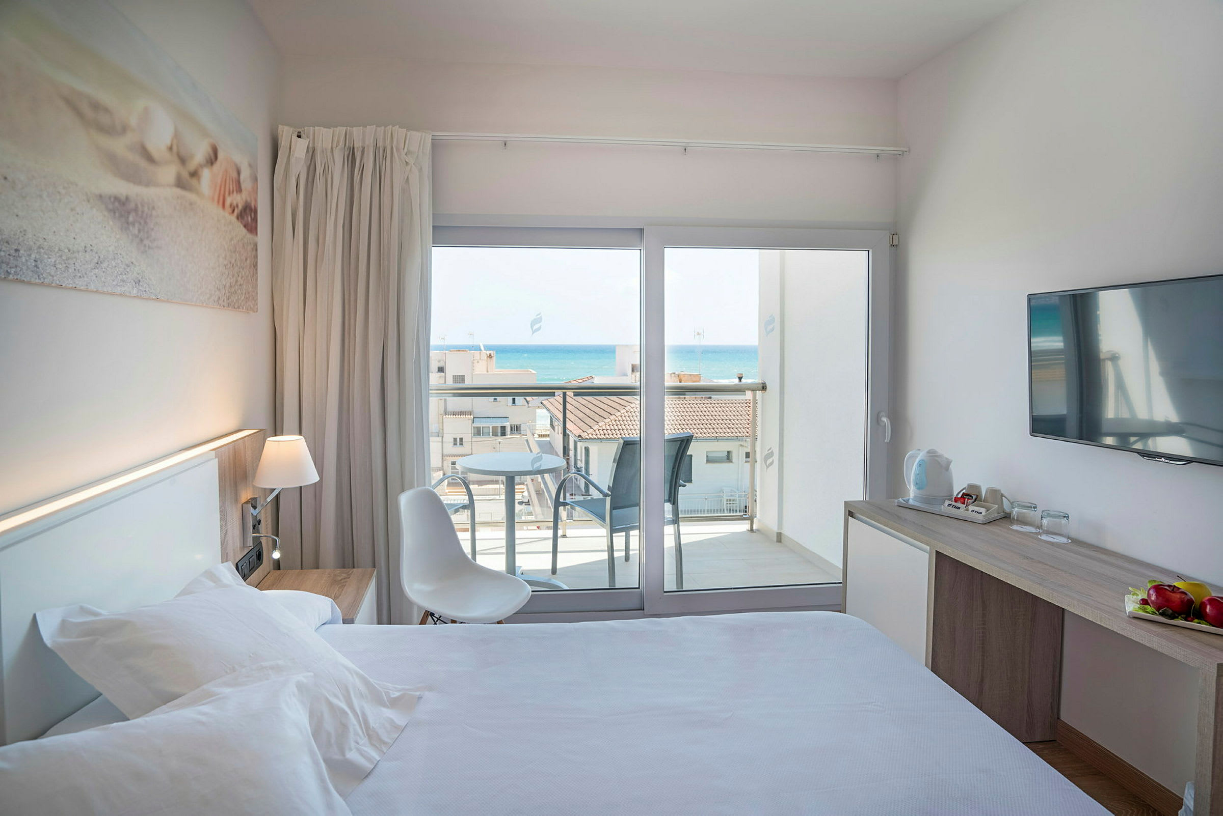 Ett hotellrum med säng, skrivbord och en balkong med utsikt över havet. (AI-genererad text)
