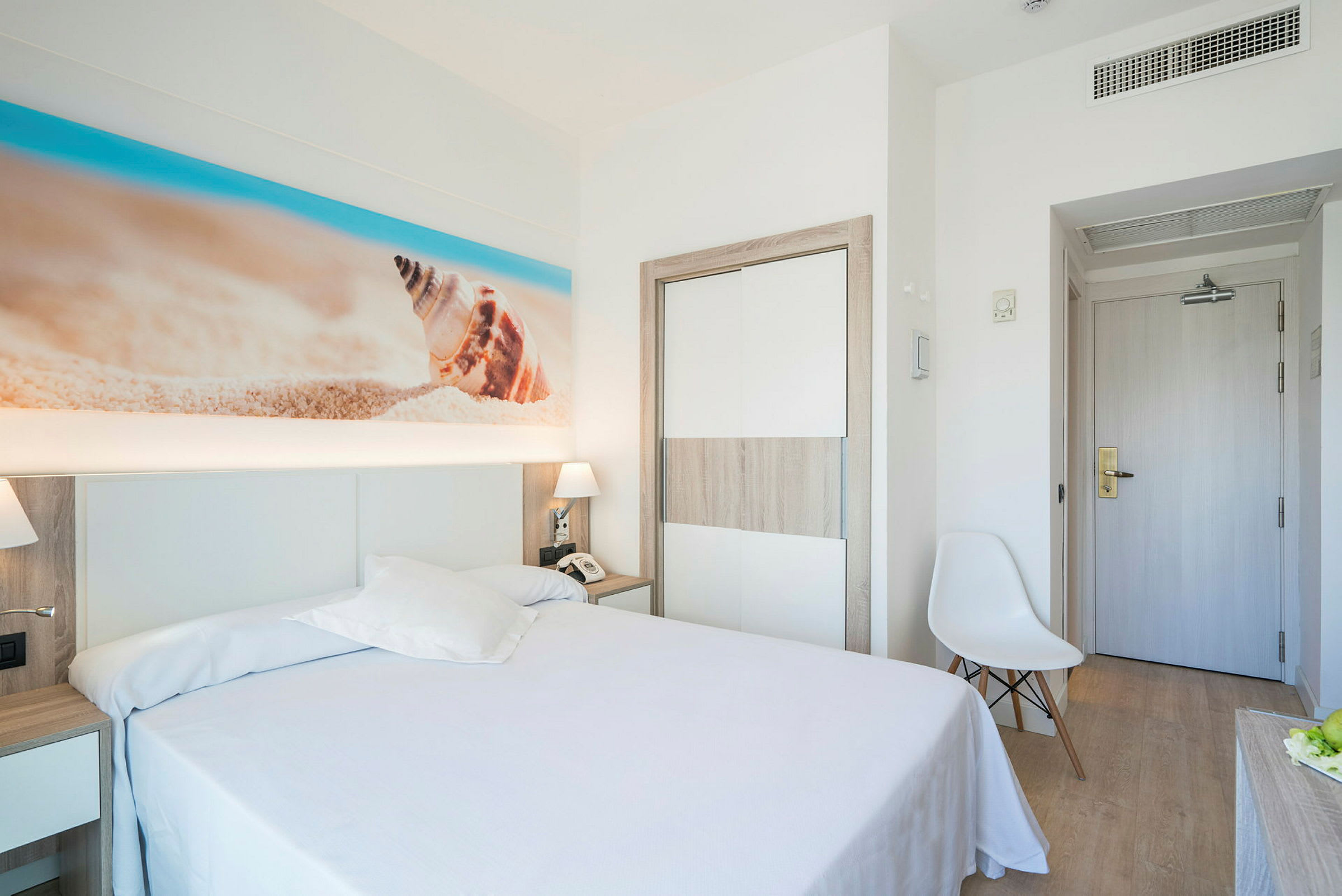 Ett hotellrum med en dubbelsäng och strandinspirerat konstverk på väggen. (AI-genererad text)