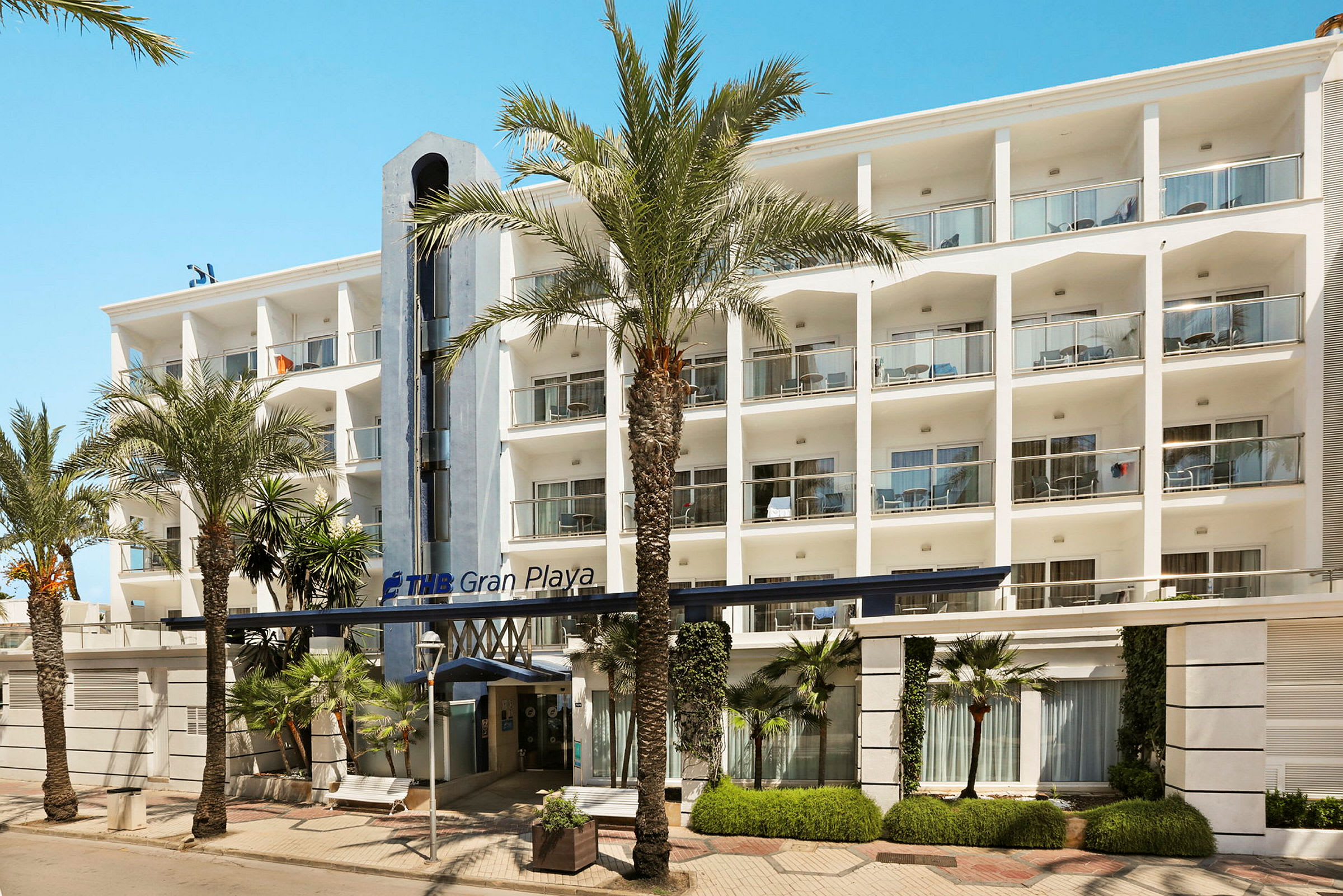Hotellbyggnad med tre våningar och balkonger framför, omgiven av palmer. (AI-genererad text)