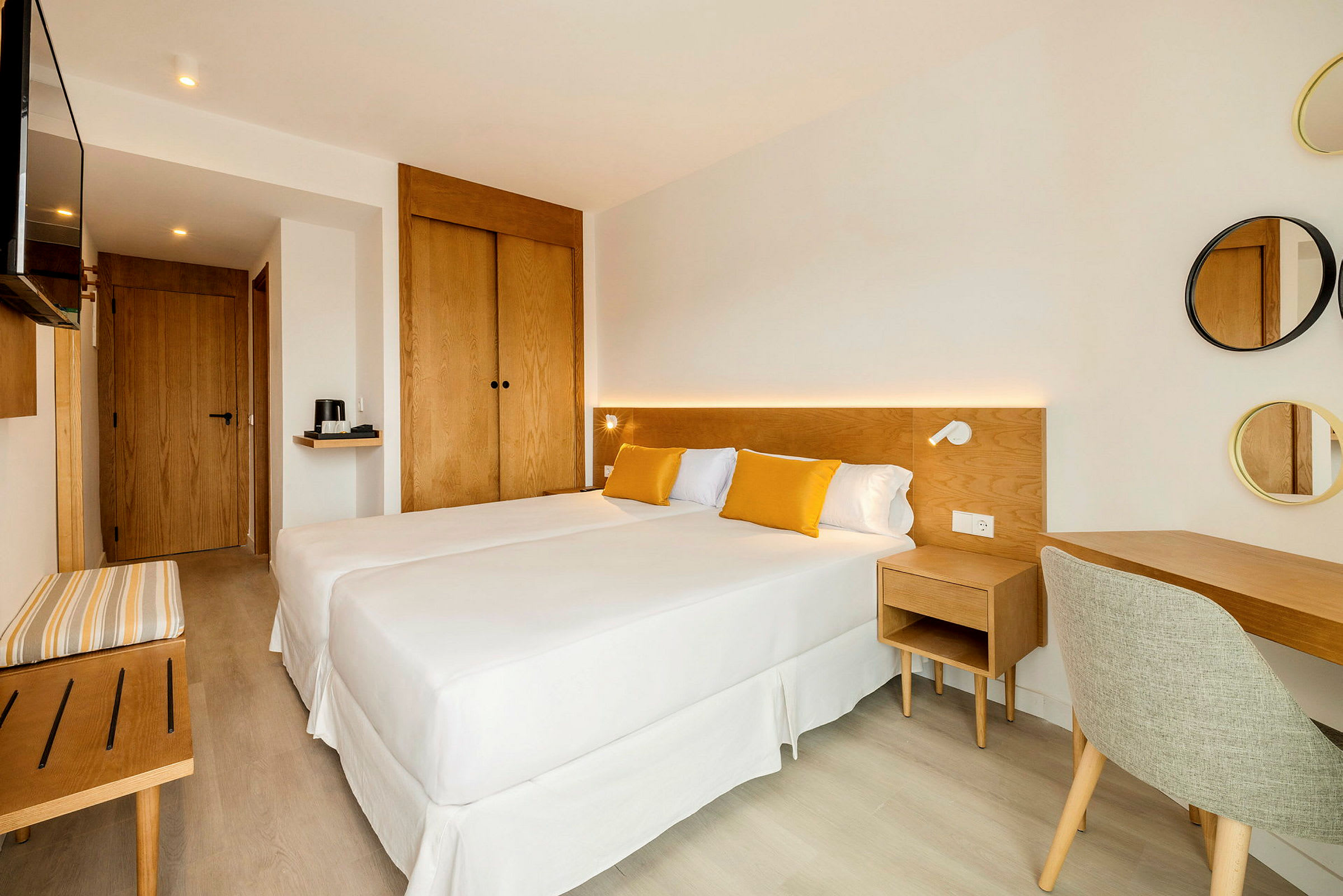 Ett ljust och modernt inrett hotellrum med två enkelsängar, trämöbler och gulddetaljer i textilier. (AI-genererad text)