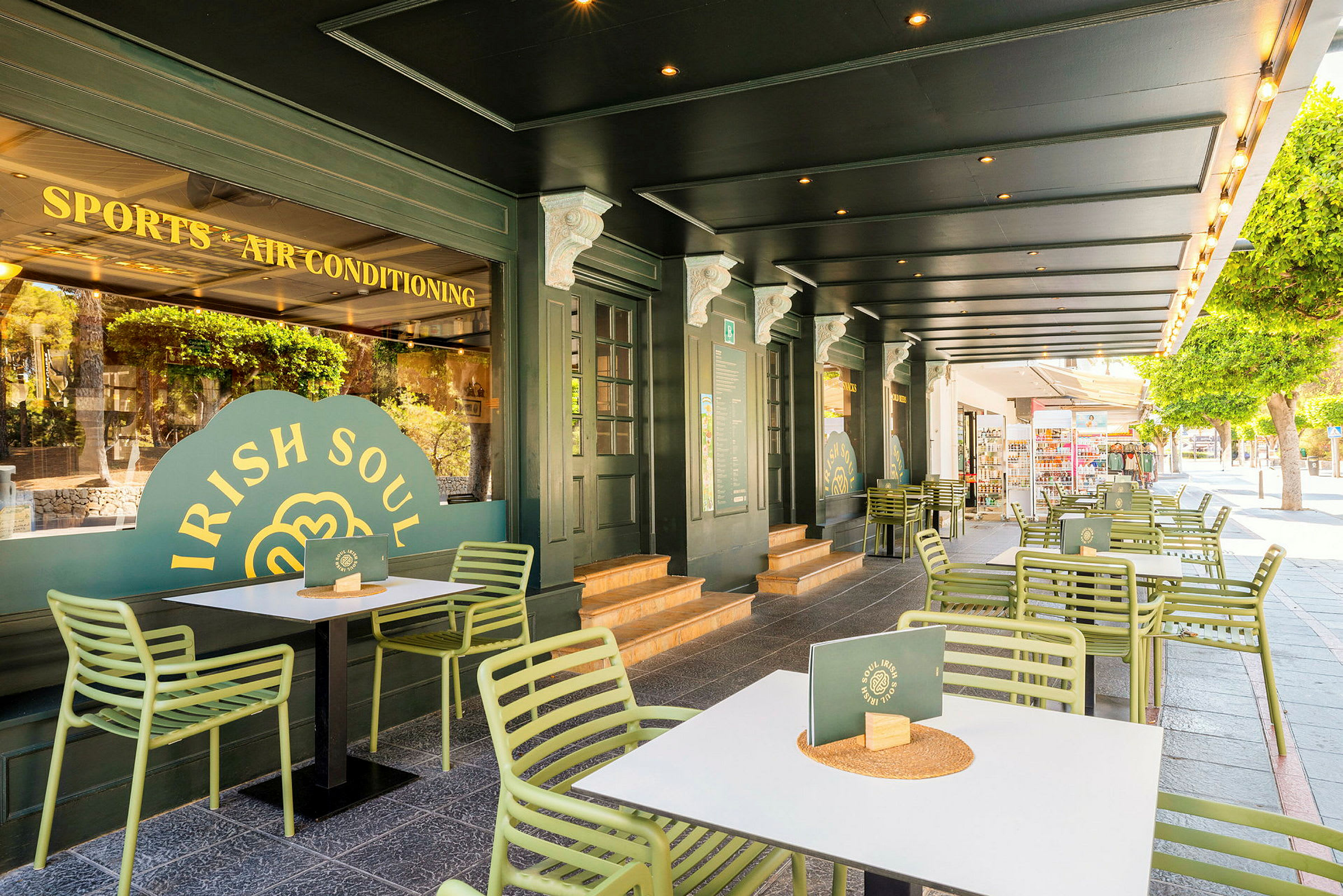 Uteservering med gröna stolar och vita bord framför en restaurang med grön fasad. (AI-genererad text)