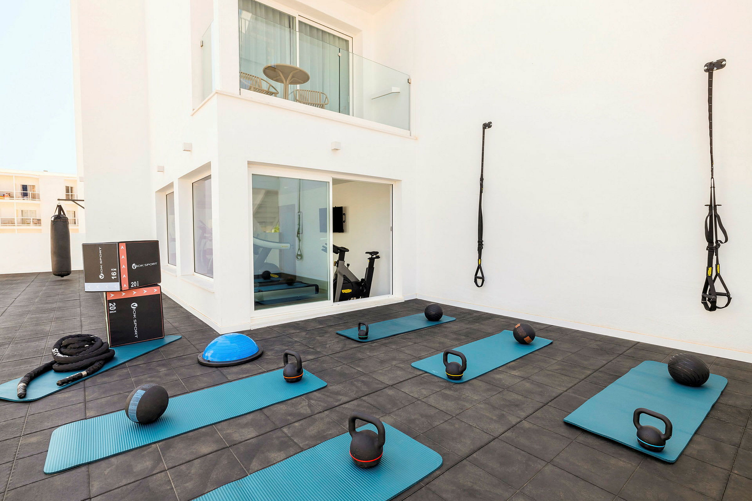 En utomhusträningsyta med träningsmattor, kettlebells, medicinbollar och TRX-band samt en boxningssäck. (AI-genererad text)
