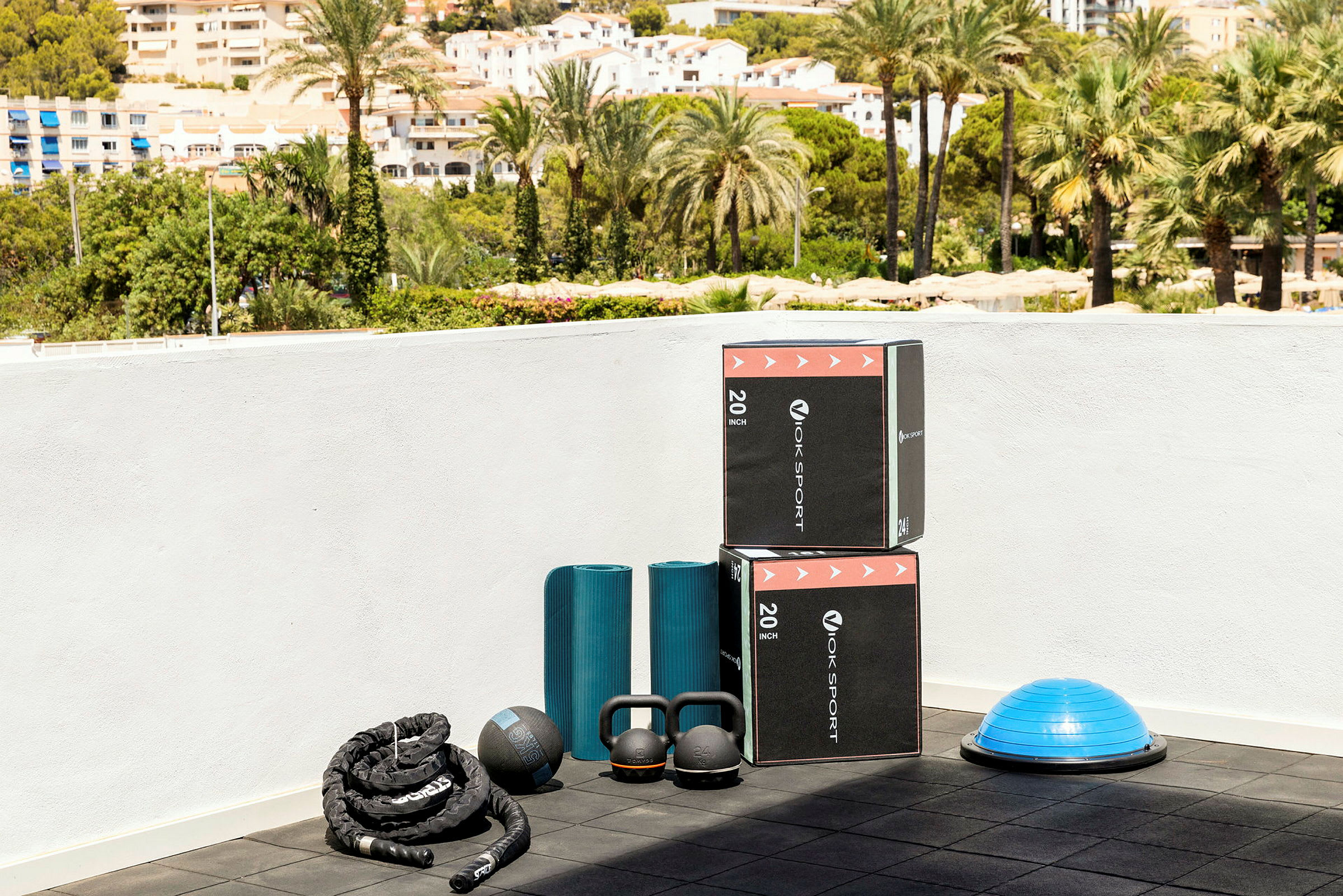 Träningsutrustning inklusive boxar, träningsmattor, kettlebells och en balansboll på en uteplats. (AI-genererad text)