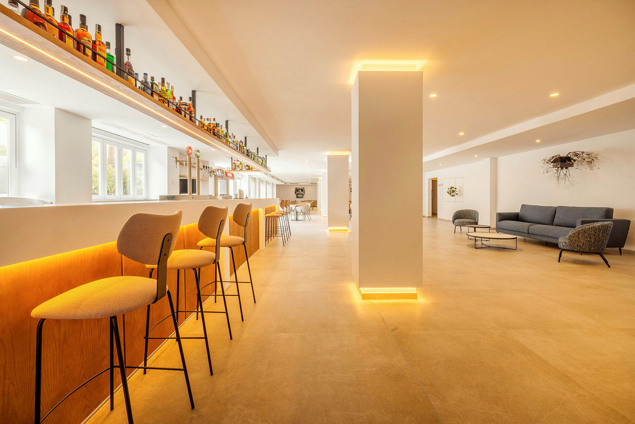 En modern bar med höga stolar, ljus inredning och en loungeavdelning med soffor och bord. (AI-genererad text)