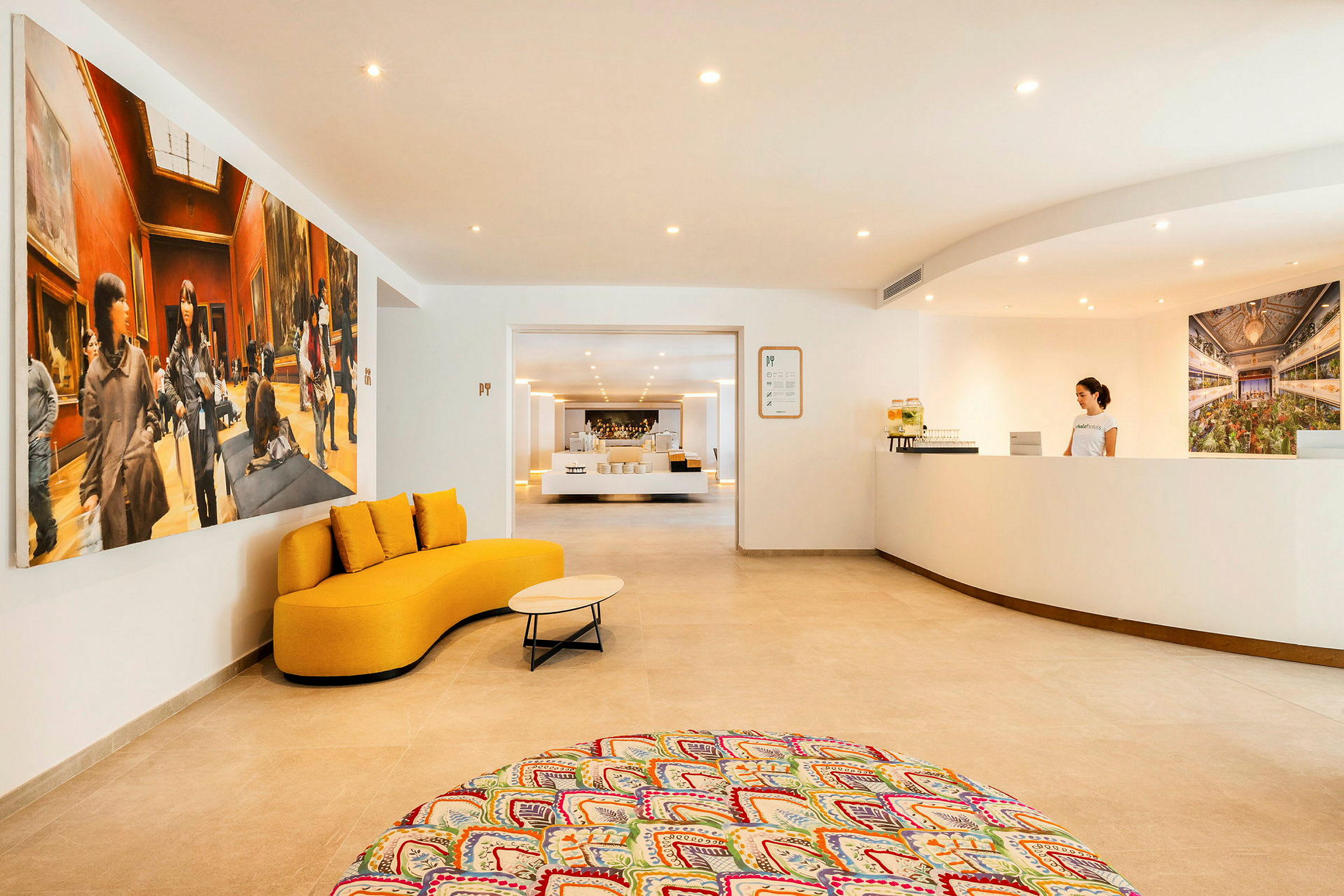 Ett hotellreceptionsområde med en vit disk, en gul soffa och färgglada mattor. (AI-genererad text)